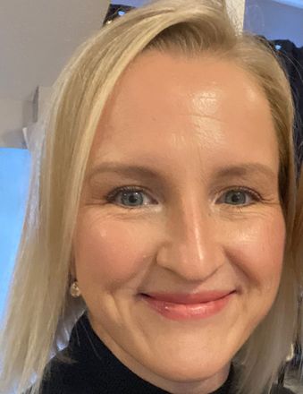 A woman with blonde hair and blue eyes is smiling for the camera.