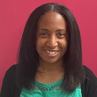 A woman in a green shirt is smiling in front of a pink background.