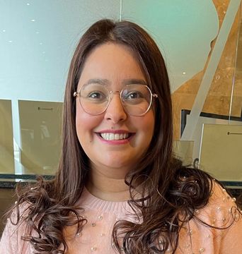 A woman wearing glasses and a pink sweater is smiling for the camera.