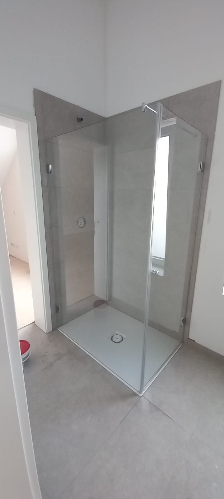 Box doccia angolare in vetro, in un bagno con pavimento piastrellato e pareti bianche