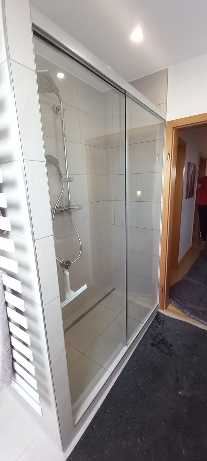 Box doccia in vetro in un bagno, accanto a uno scaldasalviette e alla porta del corridoio