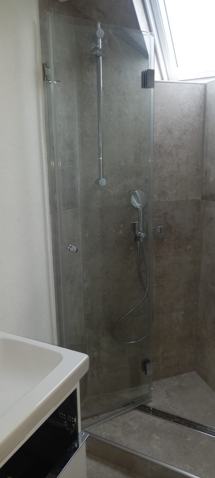 Box doccia in vetro con doccetta a mano in un bagno piastrellato