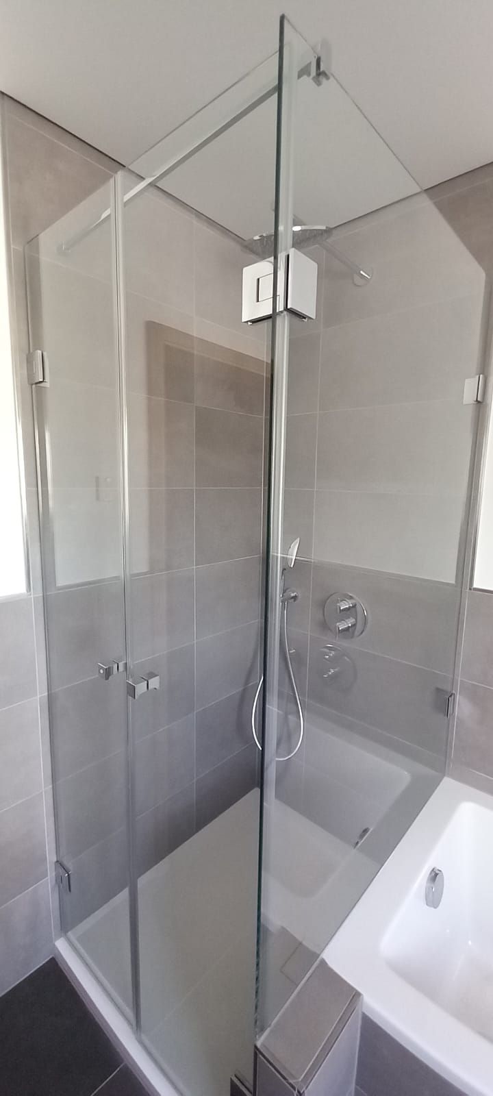 Box doccia in vetro con ferramenta cromata accanto a una vasca bianca in un bagno piastrellato
