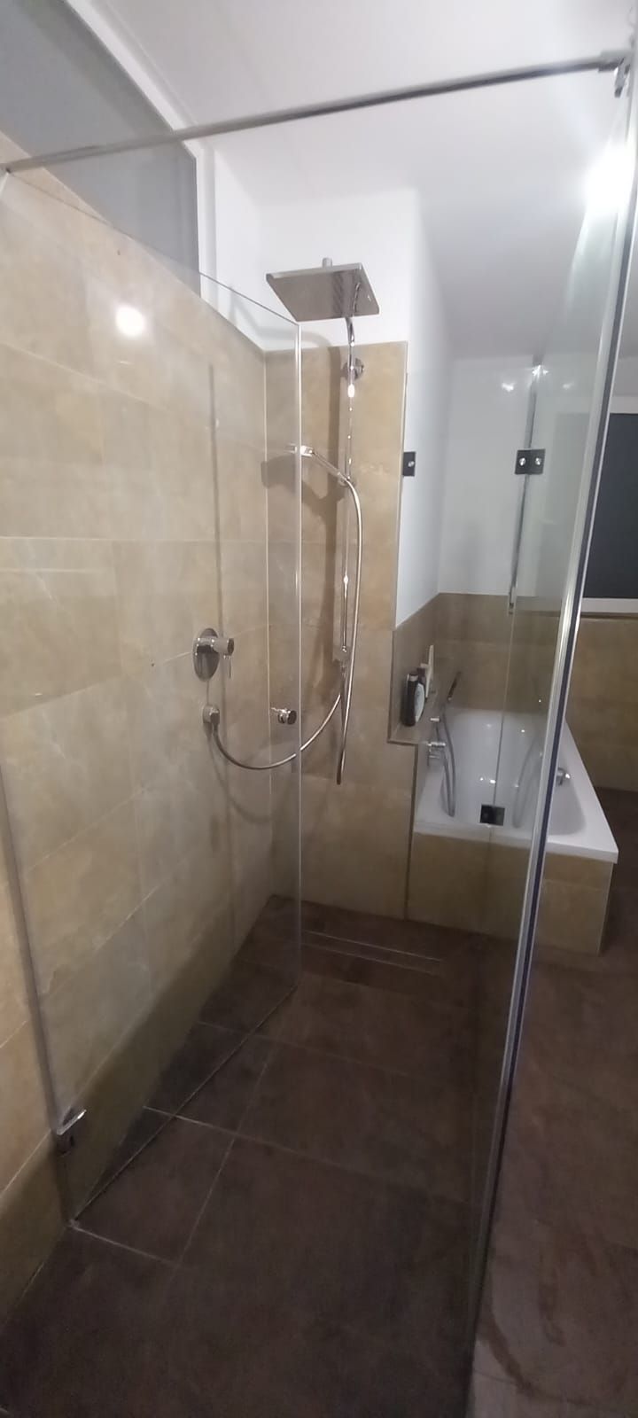 Stretto box doccia piastrellato con doccetta, parete in vetro e lavabo a parete in un bagno