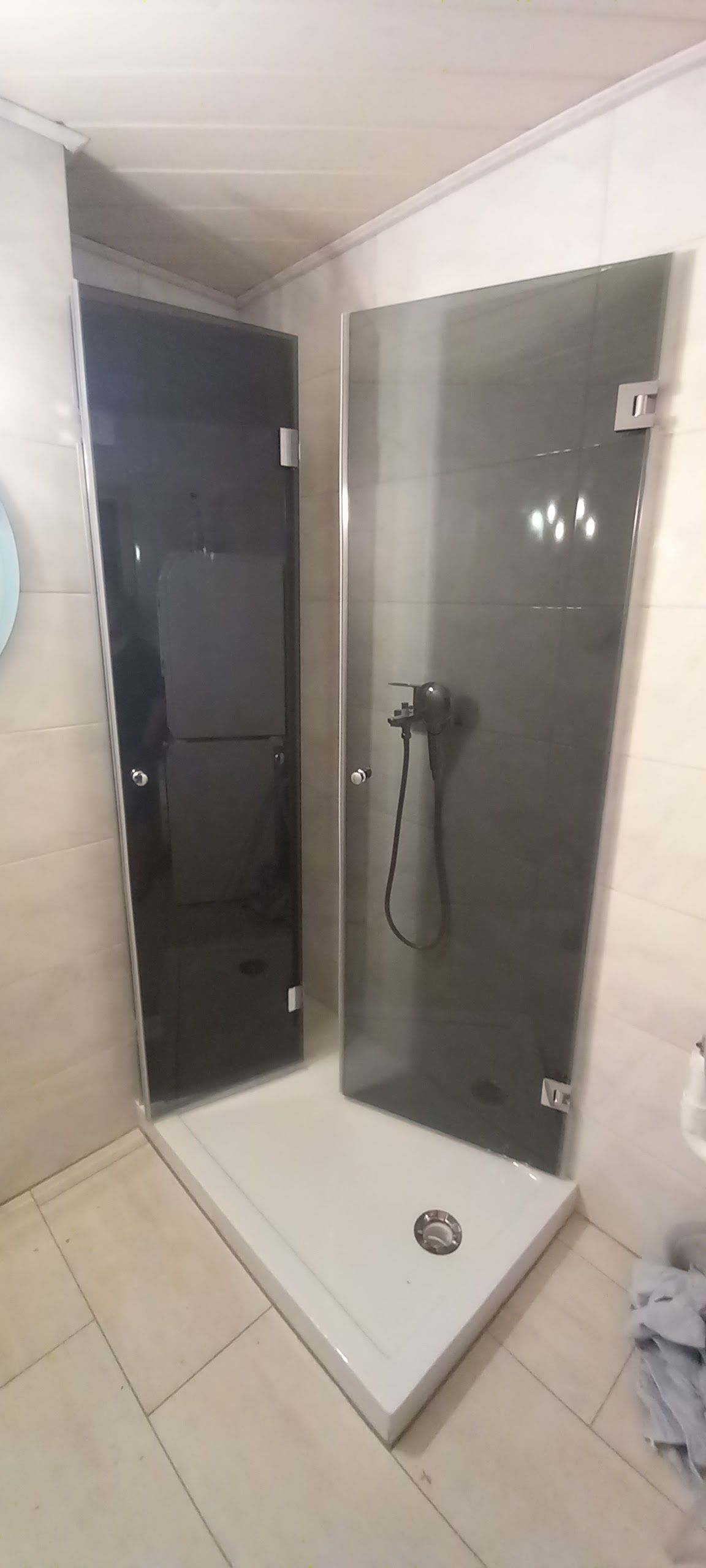 Doccia ad angolo con porta in vetro in un bagno rivestito di piastrelle bianche
