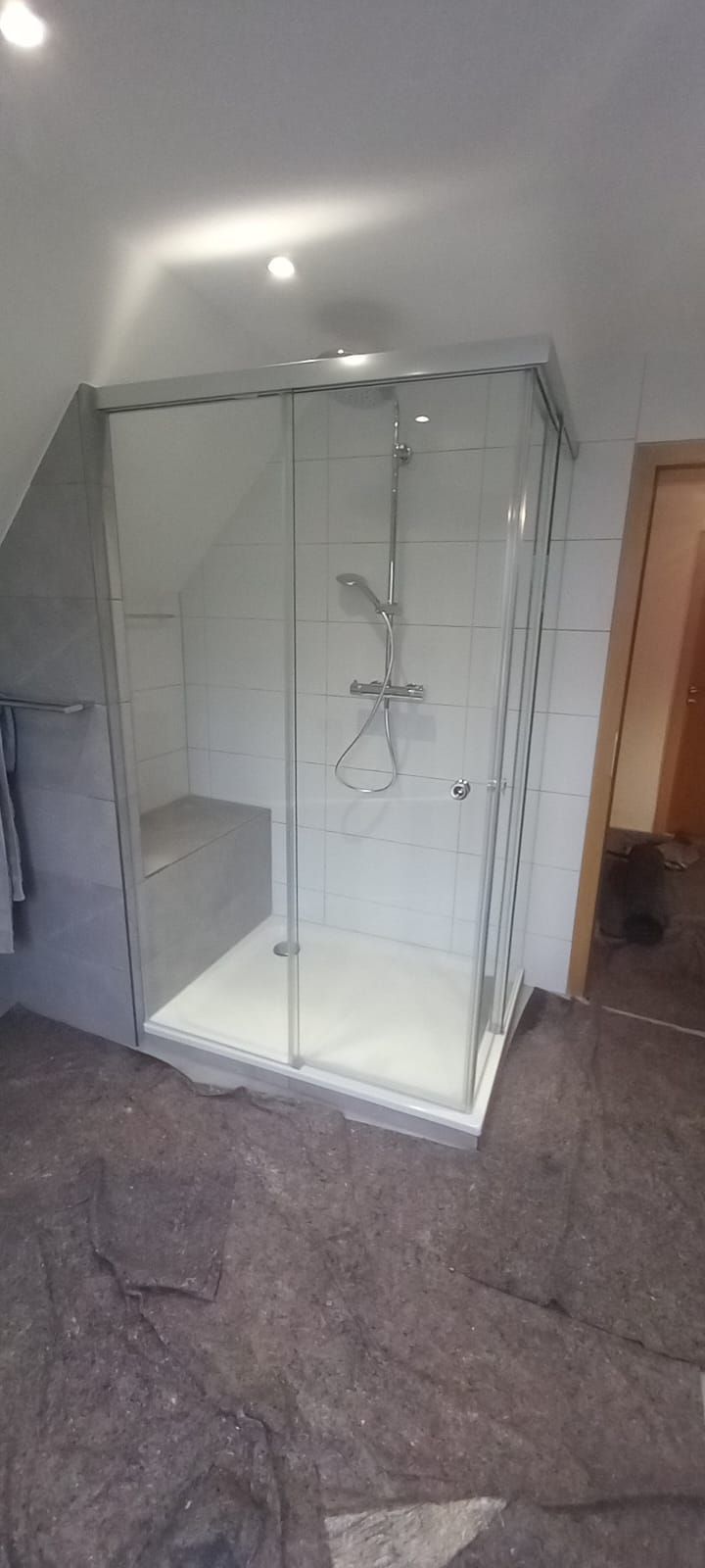 Box doccia in vetro in un bagno piastrellato, con piatto bianco e profili argentati.