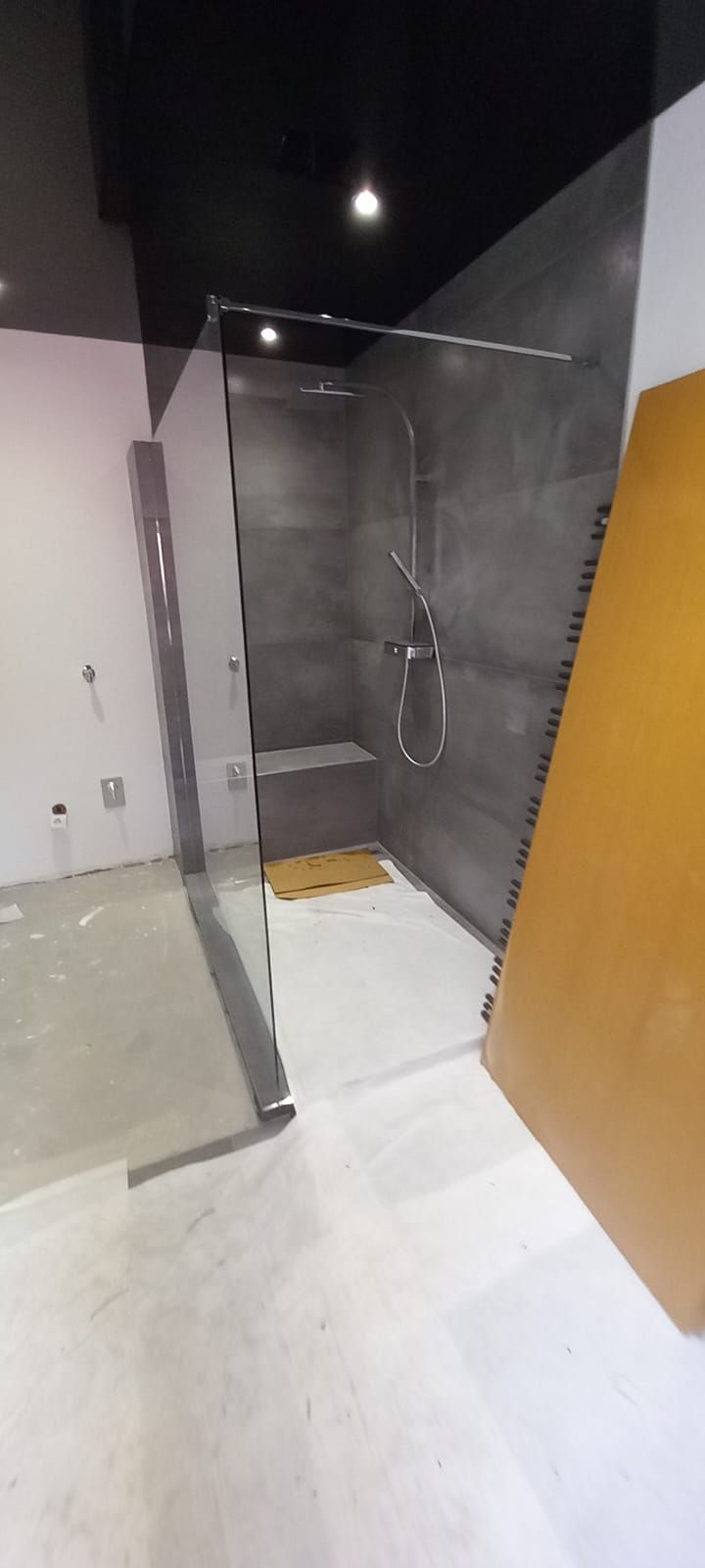 Moderna doccia a filo pavimento con box in vetro, piastrelle grigie e pavimento del bagno bianco.