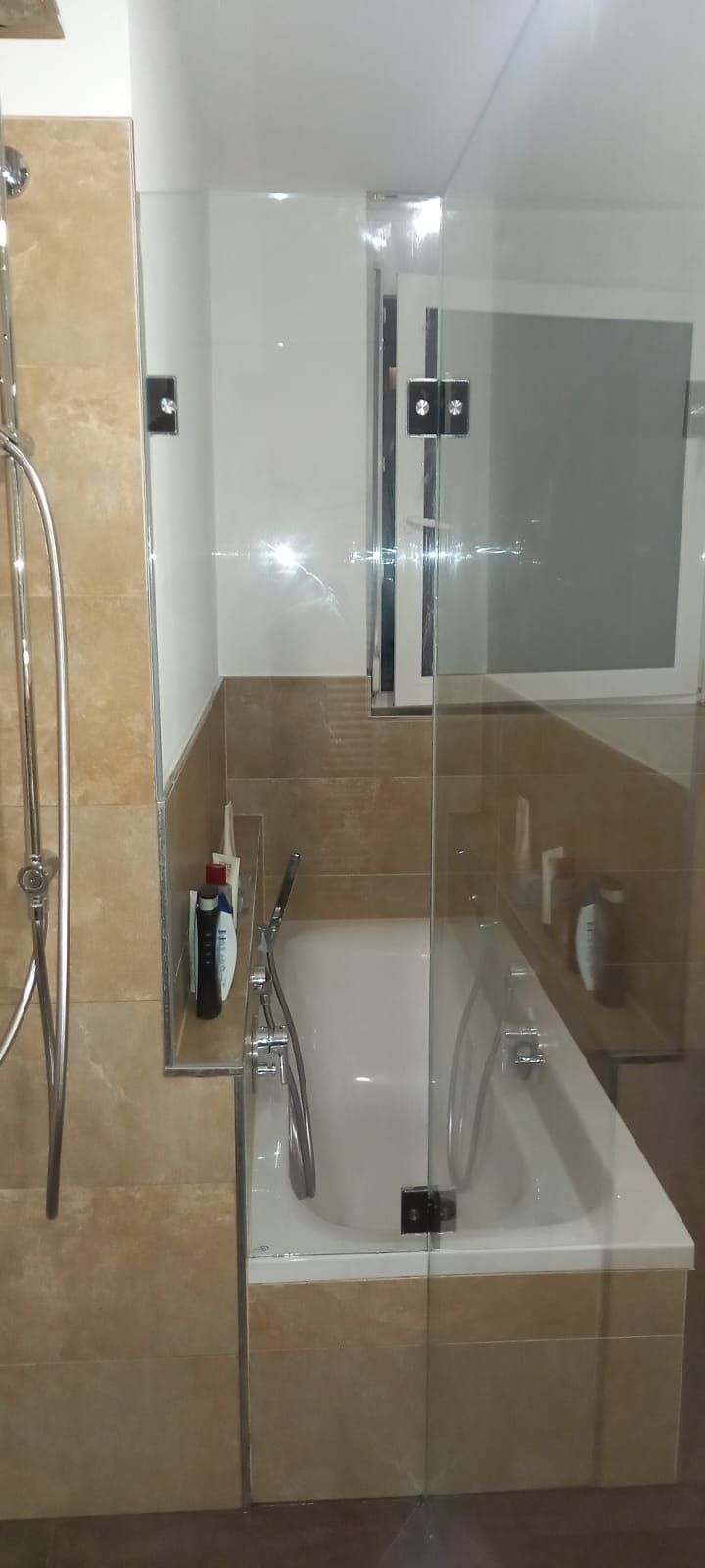 Box doccia in vetro con vasca bianca e pareti del bagno rivestite con piastrelle beige