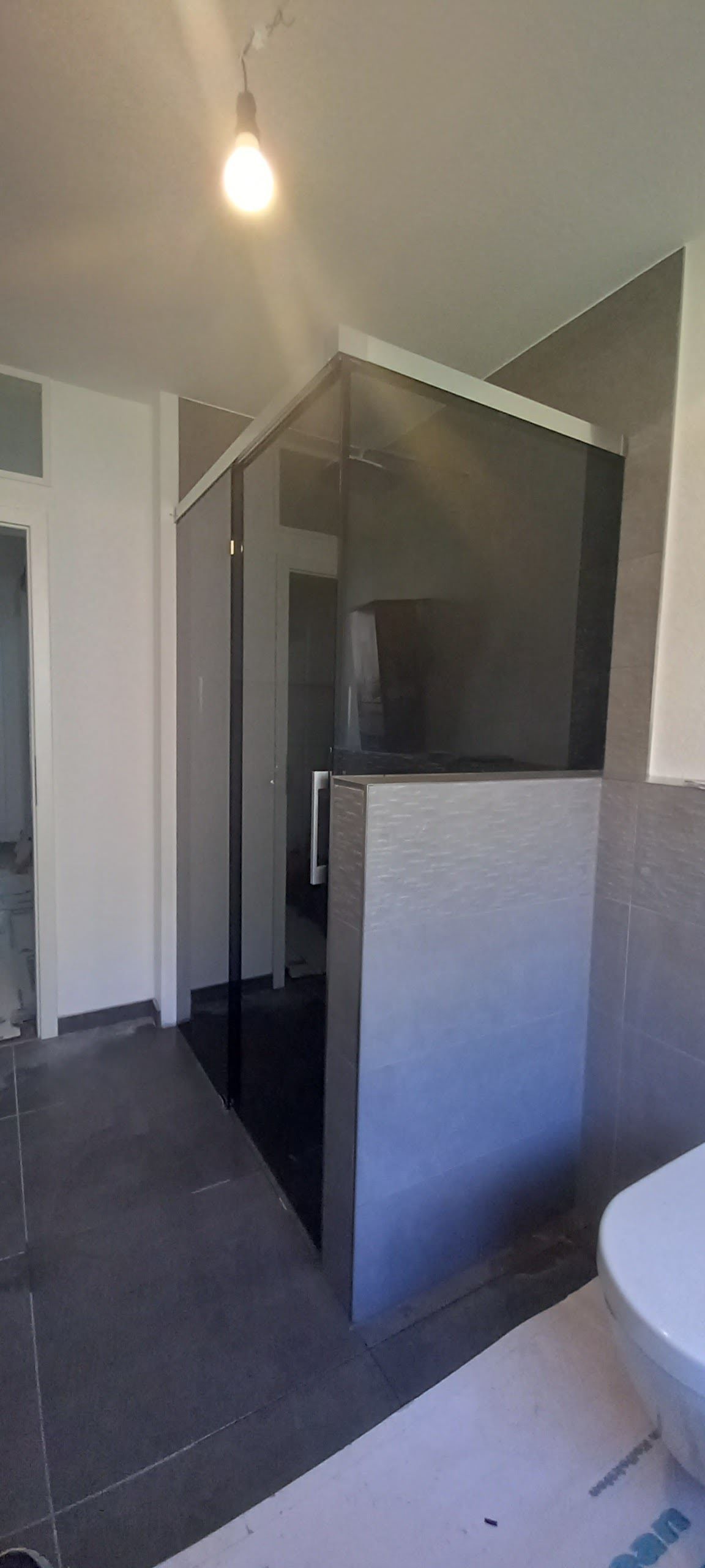 Box doccia moderno con piastrelle scure e parete divisoria in vetro satinato in un bagno