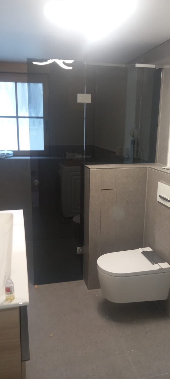 Bagno piccolo con WC sospeso, pavimento grigio e box doccia in vetro.