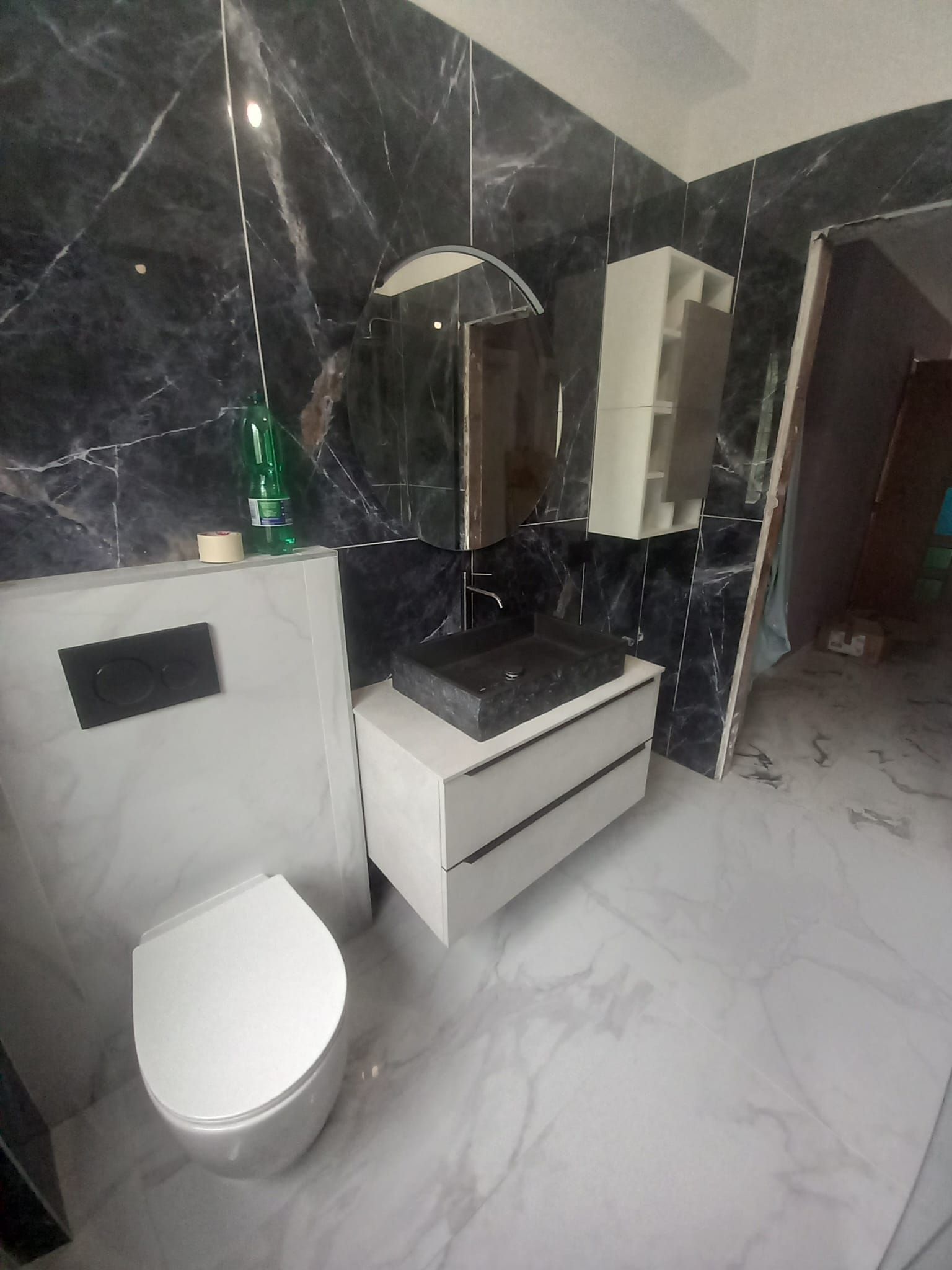 Bagno moderno con pareti in marmo nero, WC bianco e mobile lavabo con specchio rotondo