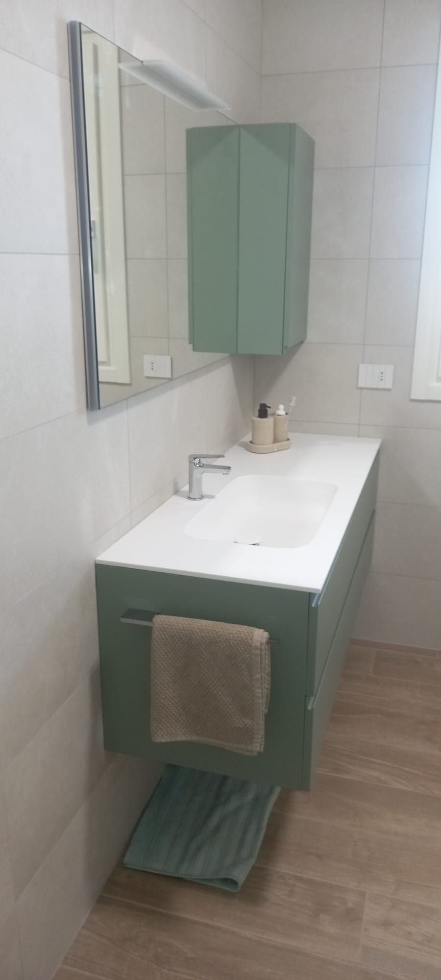 Mobile bagno moderno con ante verdi, specchio, lavabo e asciugamano beige sul davanti.