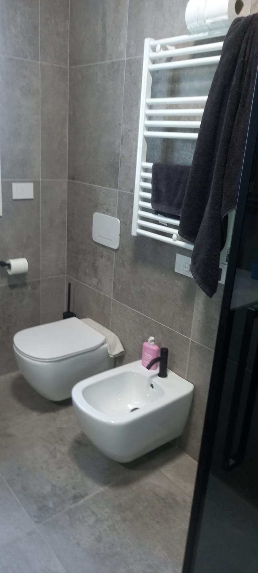 Bagno moderno con piastrelle grigie, WC sospeso, bidet, portasciugamani e asciugamani appesi