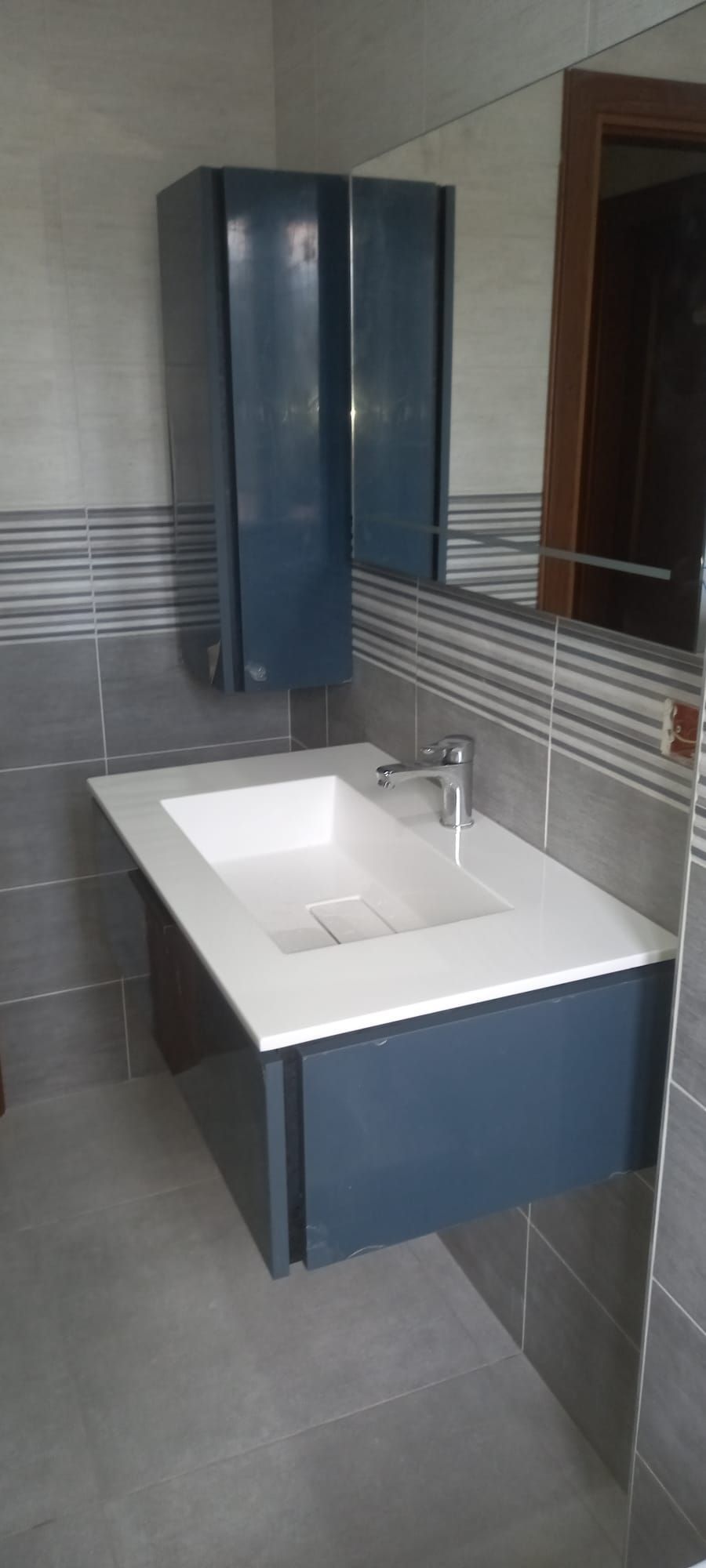Bagno moderno con piastrelle grigie, un mobile lavabo bianco e un mobile blu scuro con pannello a specchio.