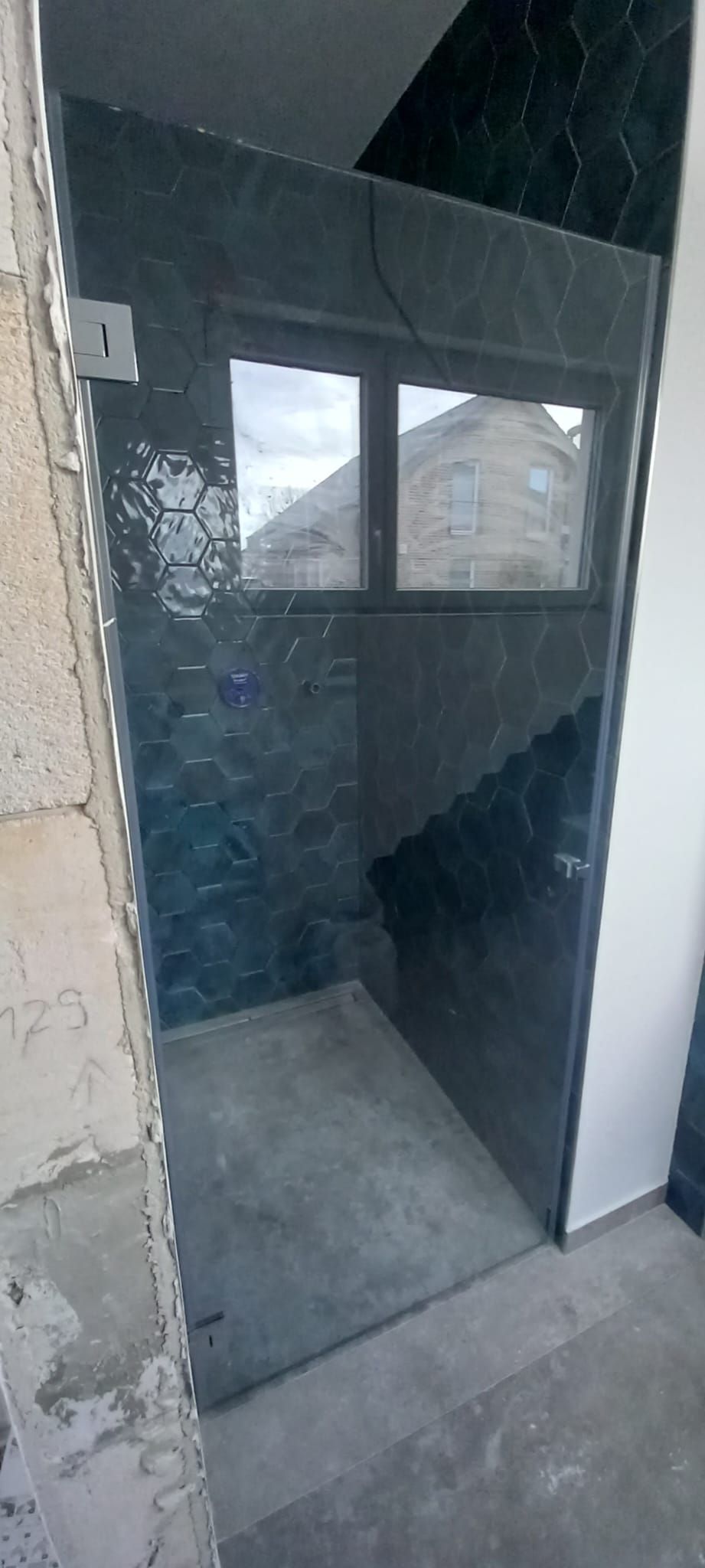 Porta aperta su una piccola stanza piastrellata, con una finestra smerigliata e l’interno buio