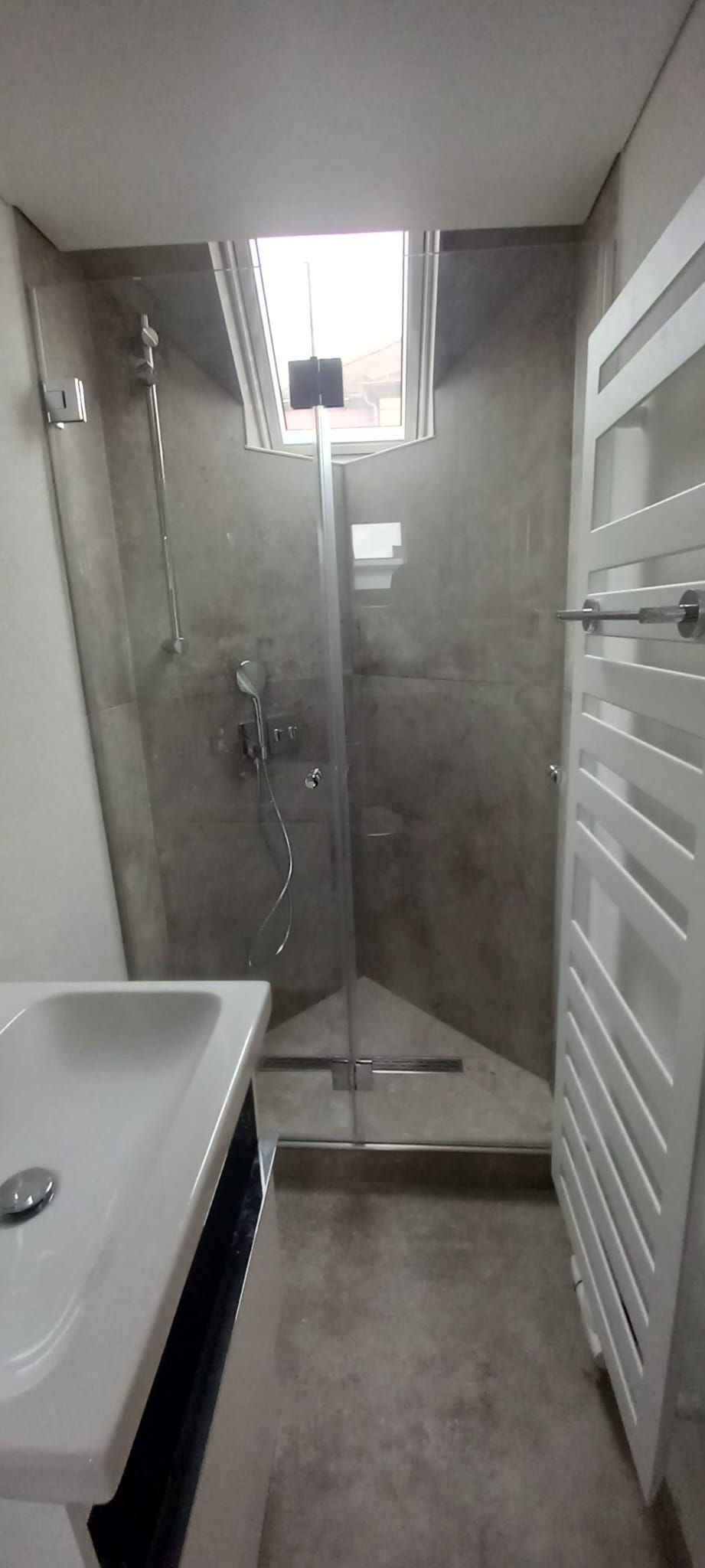 Bagno stretto con doccia, WC, lavabo e lucernario, rappresentato in tonalità di grigio.