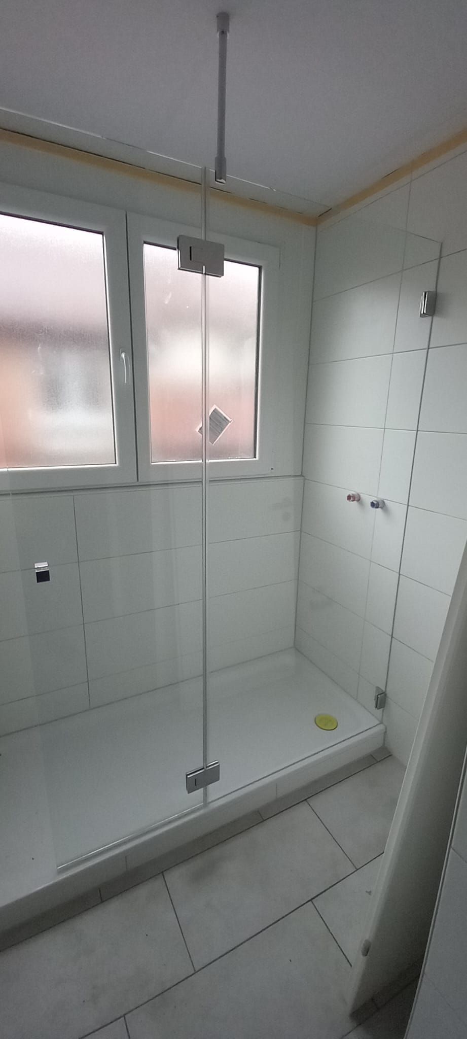Piccolo bagno piastrellato con cabina doccia in vetro, piastrelle bianche e una finestra satinata.