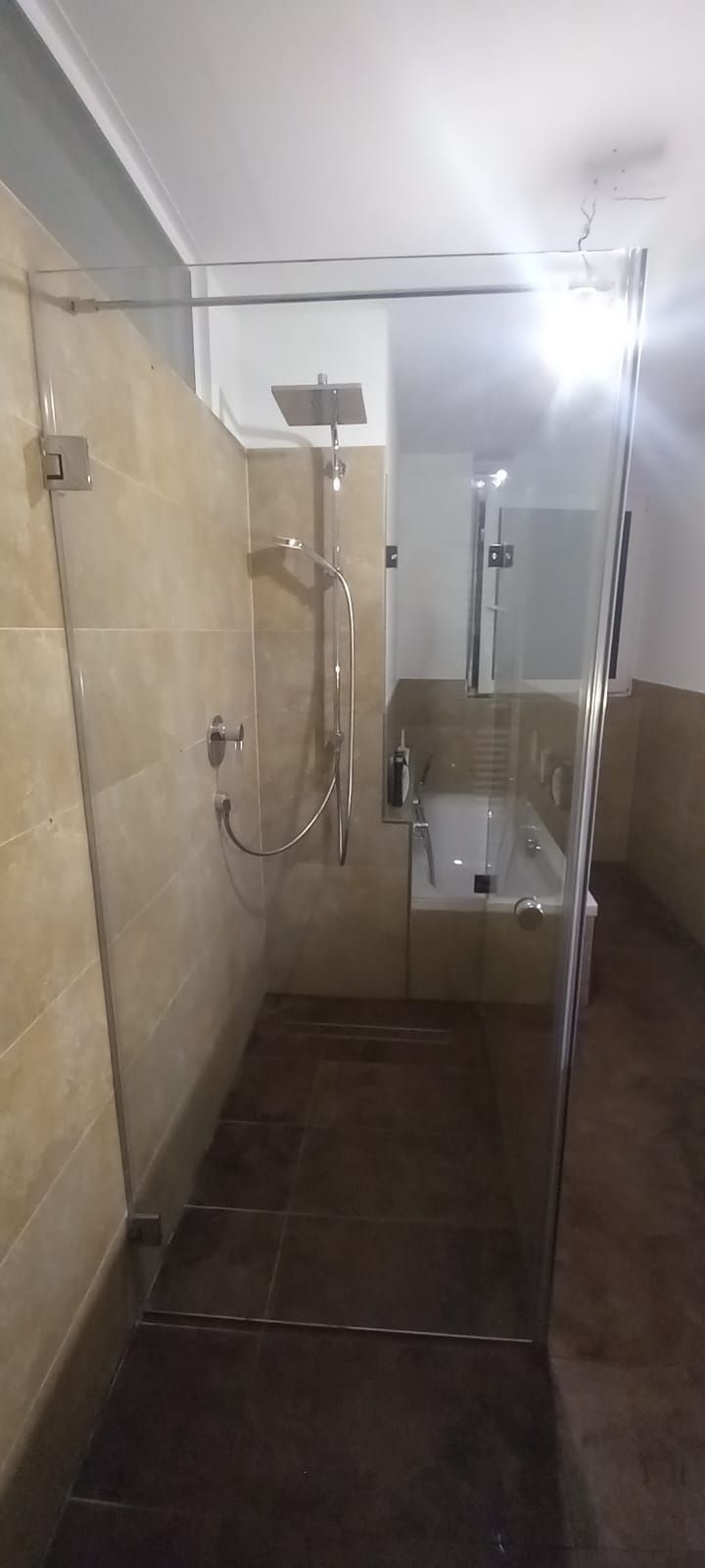 Doccia accessibile con pareti piastrellate beige, doccetta a mano e sedile a parete.
