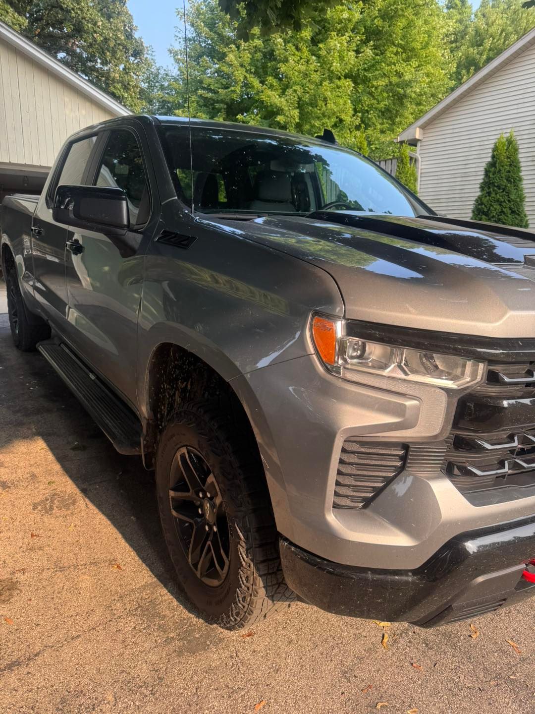 A gray Chevrolet Silverado pickup truck parked on a gravel driveway between two houses.