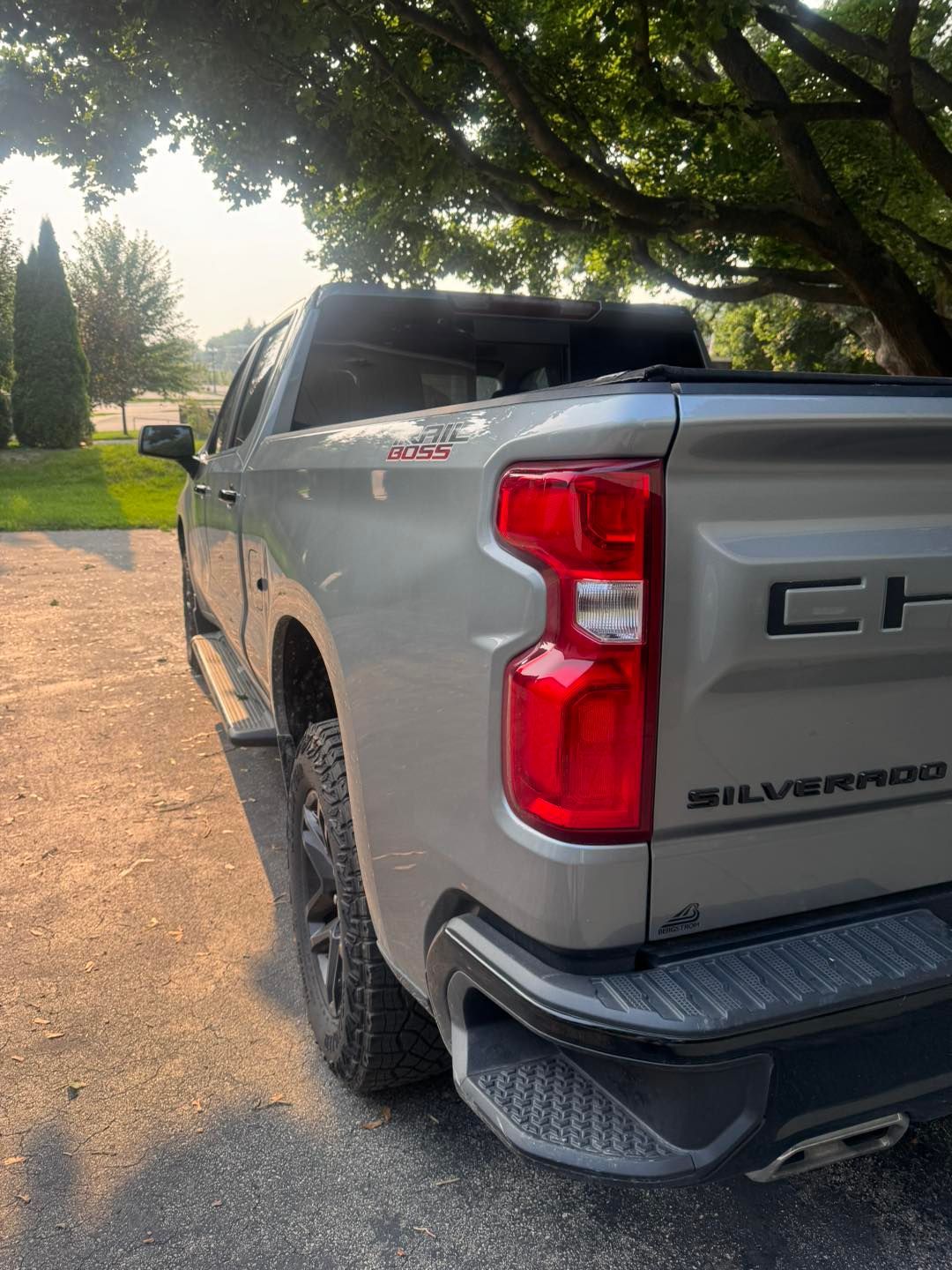 A metallic silver Chevrolet Silverado pickup truck parked outdoors, angled to show its side and rear tail light.