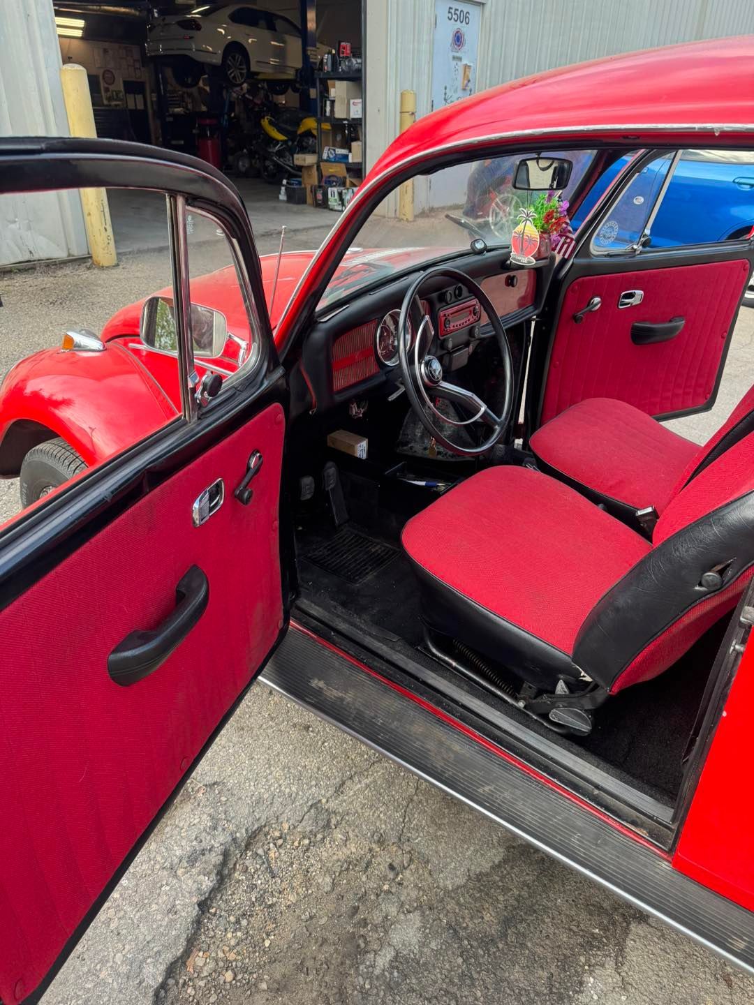 Interior of a vintage red Volkswagen Beetle with matching red upholstery and black door panels, parked in a garage.