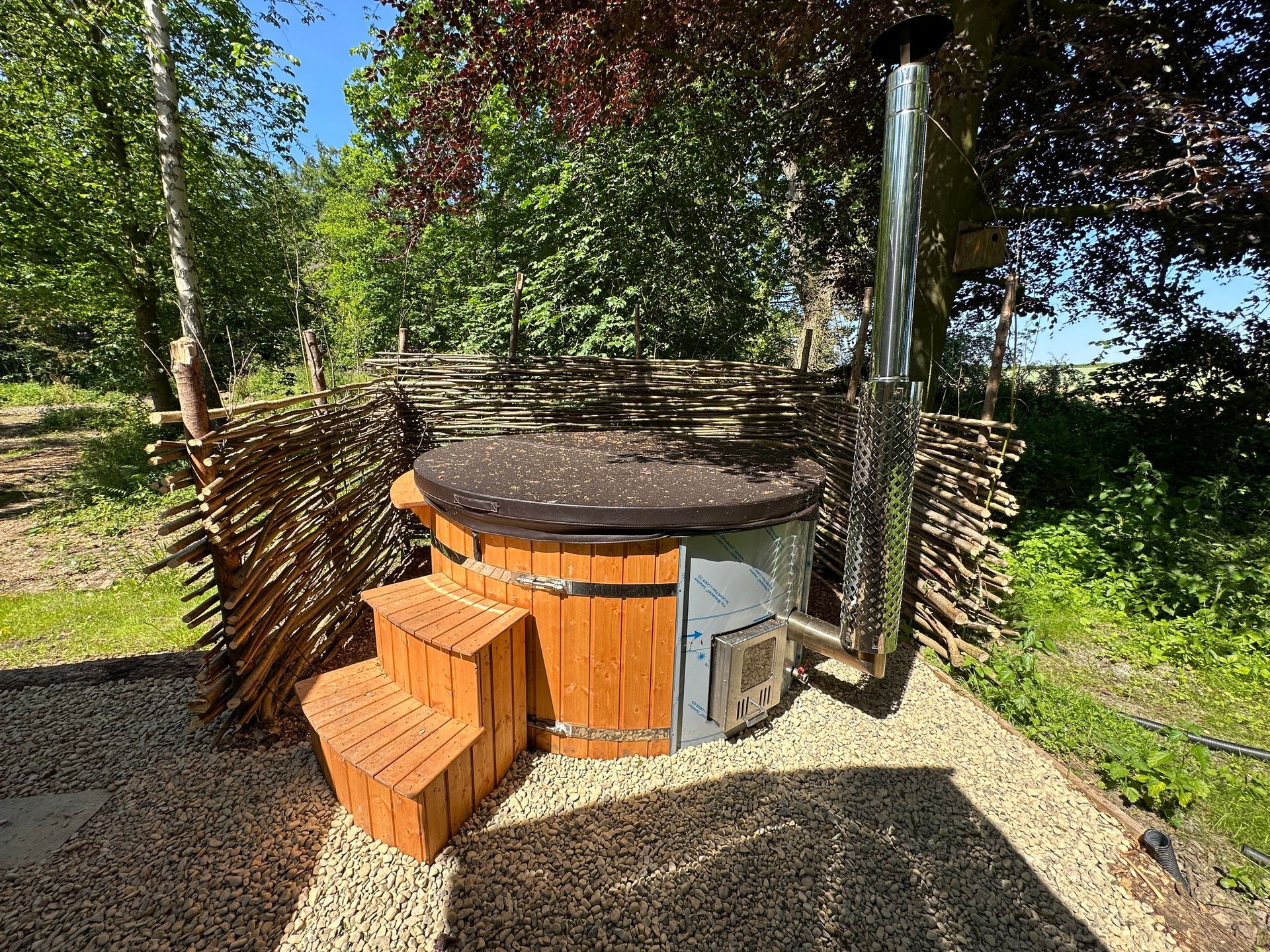 a wooden hot tub with stairs and a chimney in the woods .
