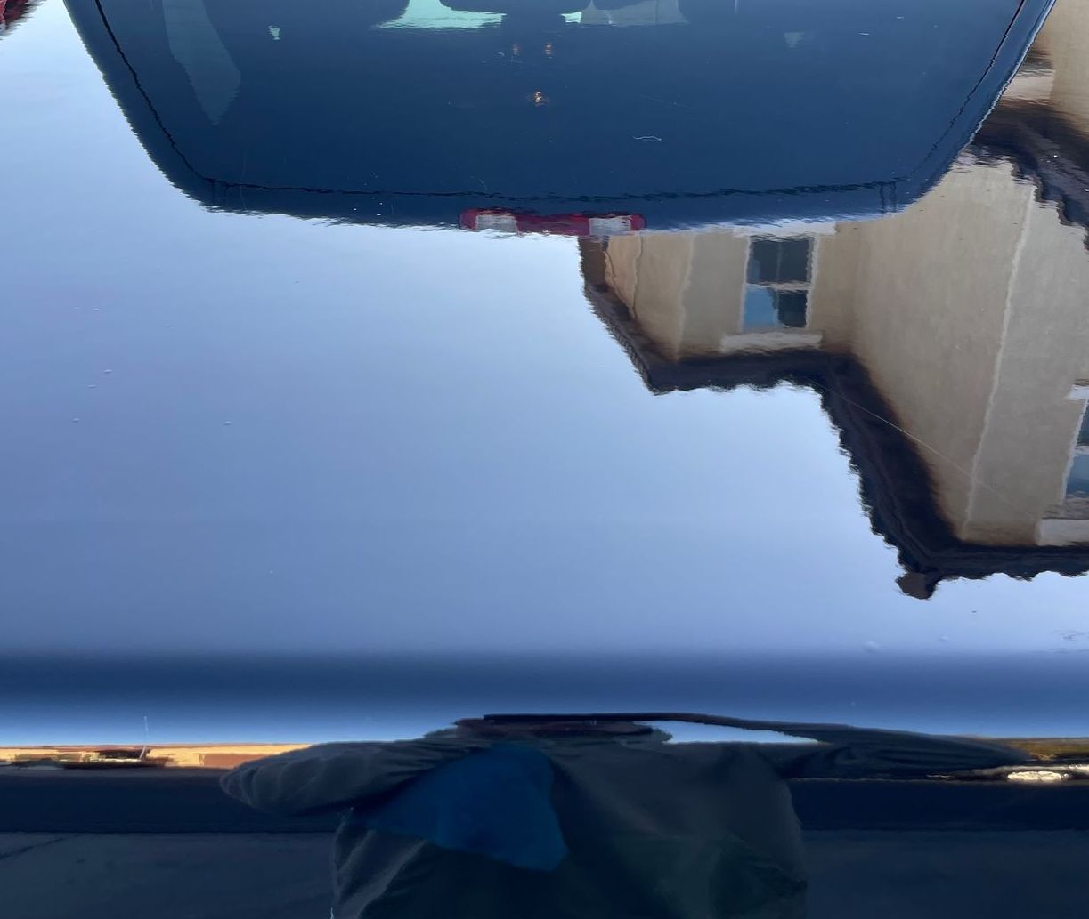 Reflection on car hood of a house and sky, with part of the car interior and windshield visible.