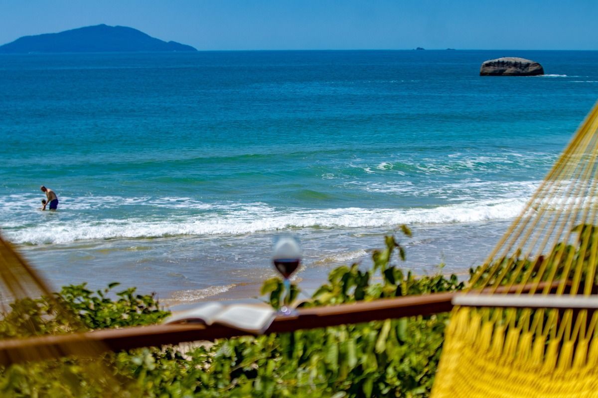 Vista da praia de uma rede, com água azul-turquesa, ondas, uma ilha ao longe e um pequeno barco no mar.