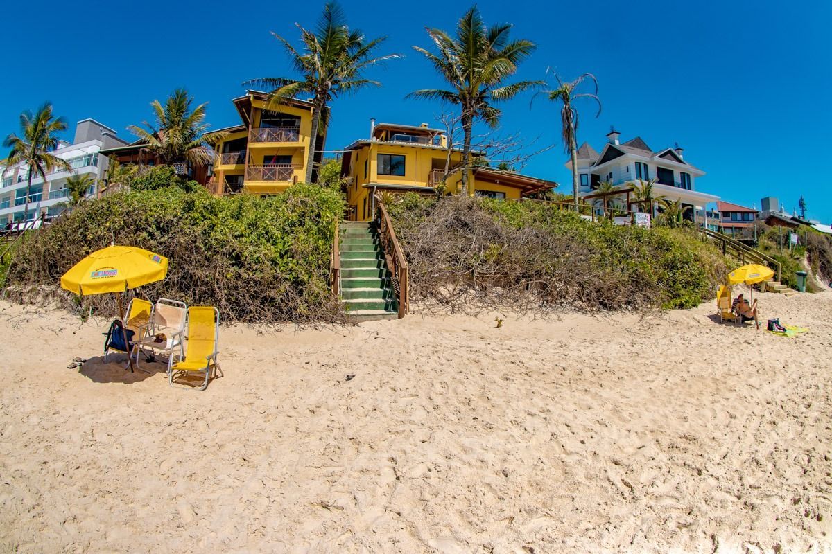 Praia de areia com casas de praia amarelas em uma falésia íngreme, uma escadaria no centro e guarda-sóis lá embaixo, sob um céu azul