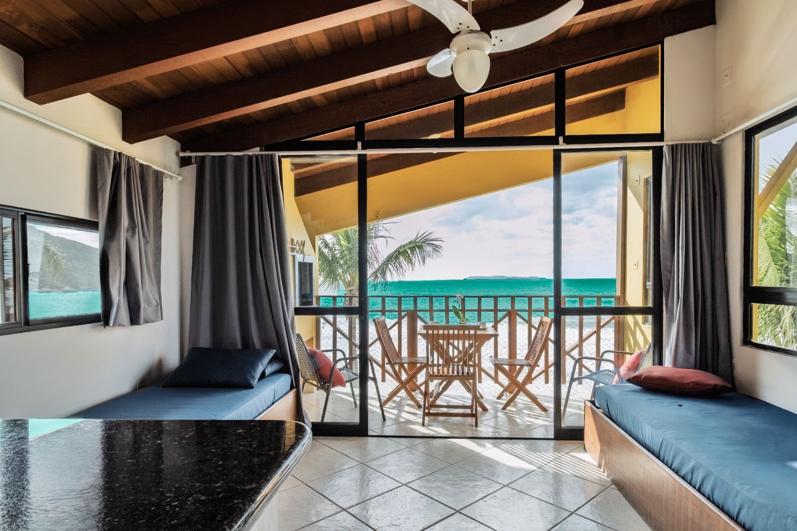 Interior de bangalô à beira-mar com duas camas de solteiro, varanda aberta e vista para o mar através das portas de correr
