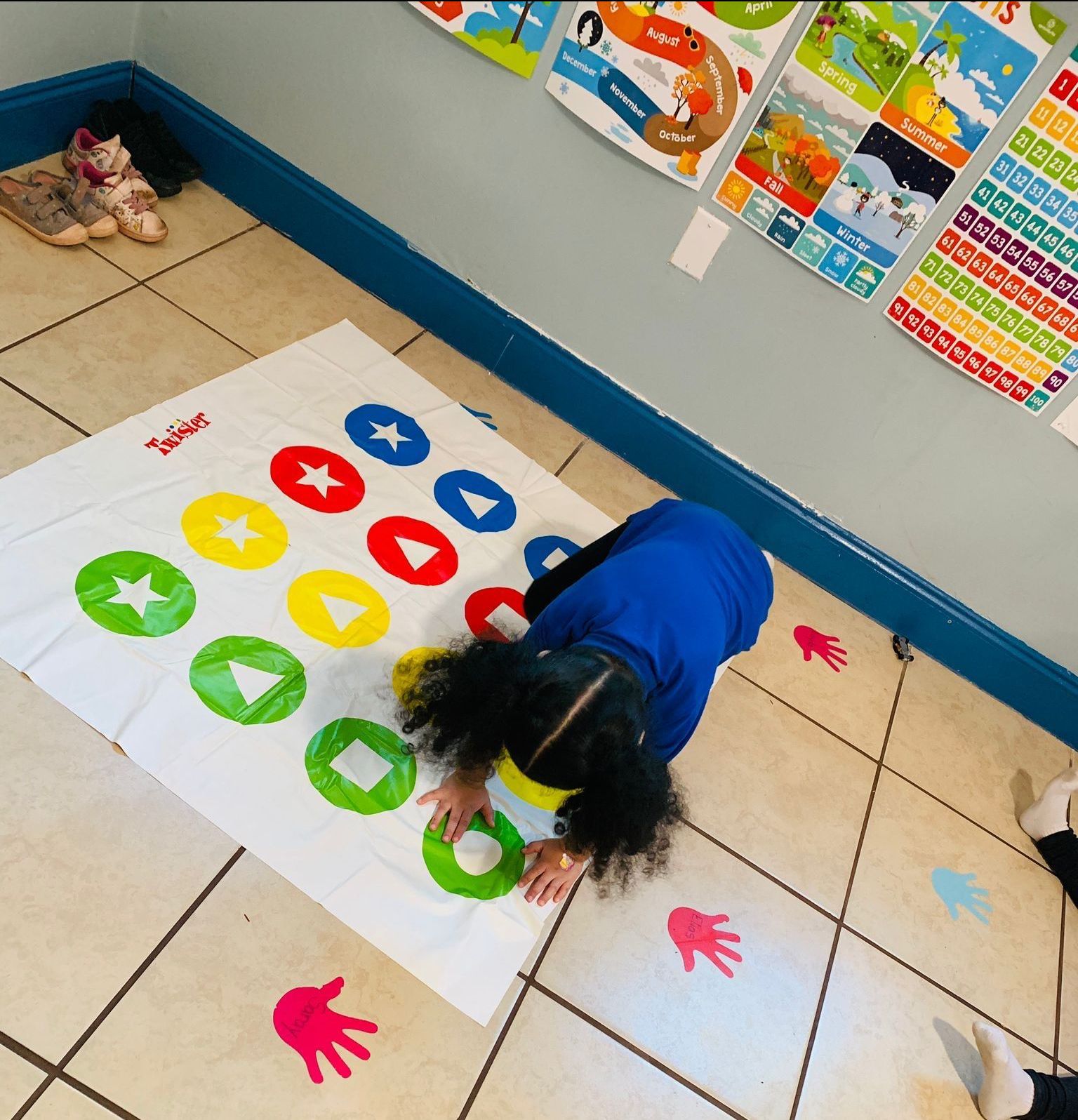 Child playing Twister game on a colorful mat with handprints on the floor.