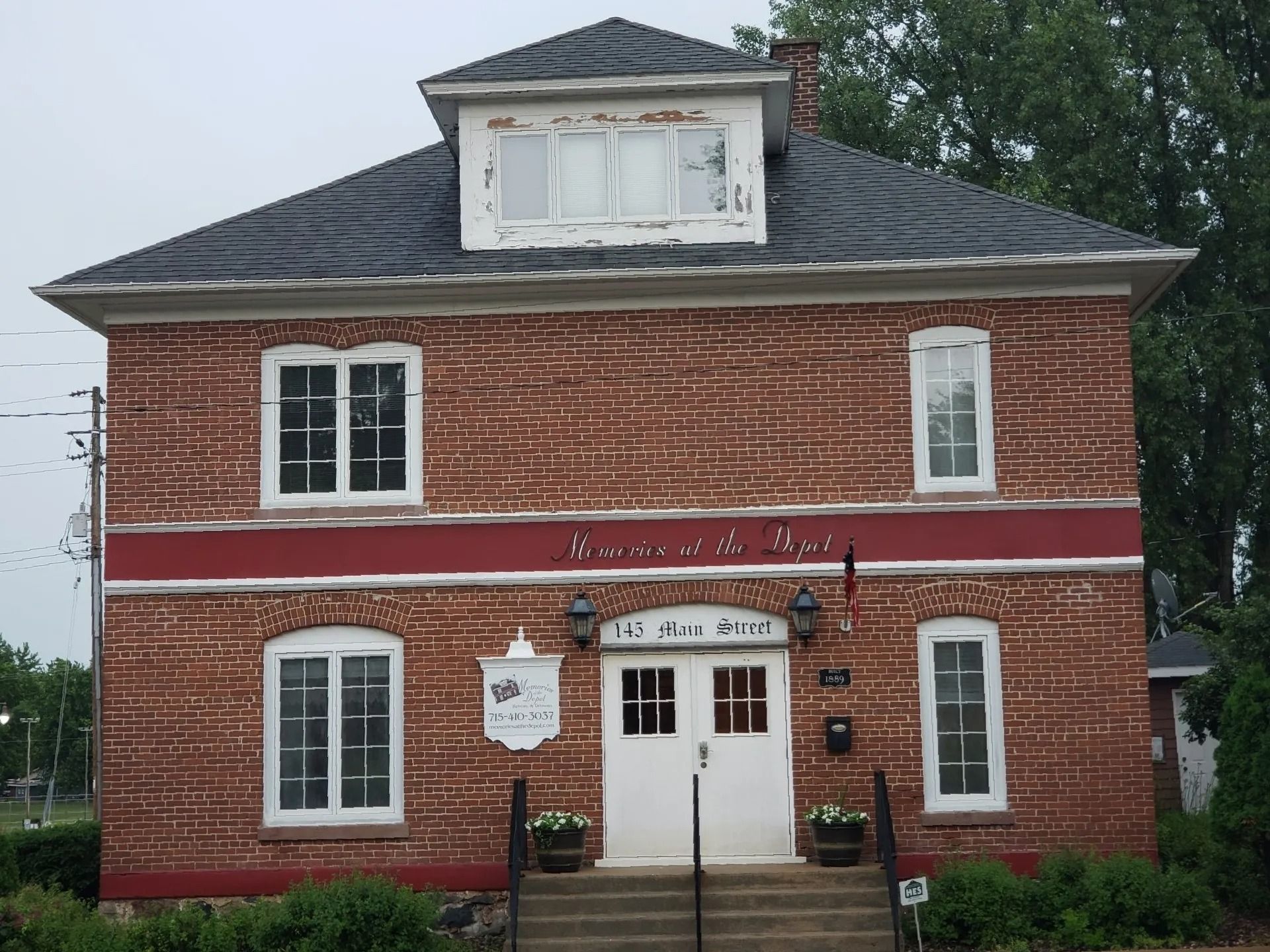 Brick building with white doors and windows, a red stripe, and a small dormer. Sign above the doors reads