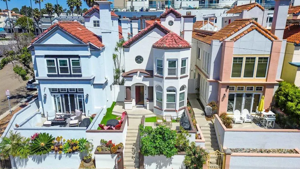 Row of colorful Victorian-style houses with red roofs and front gardens on a sunny street