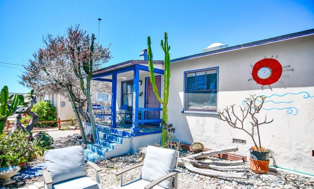 Bright desert patio with white house, blue trim, cacti, and outdoor seating under a sunny sky