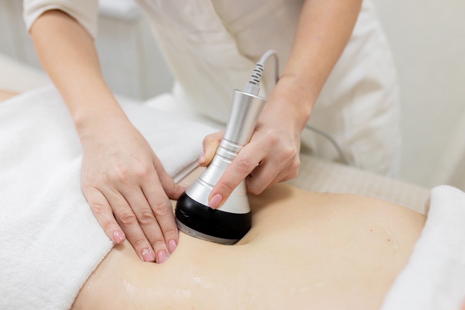 Massage therapist using a handheld device on a person’s bare back in a spa setting