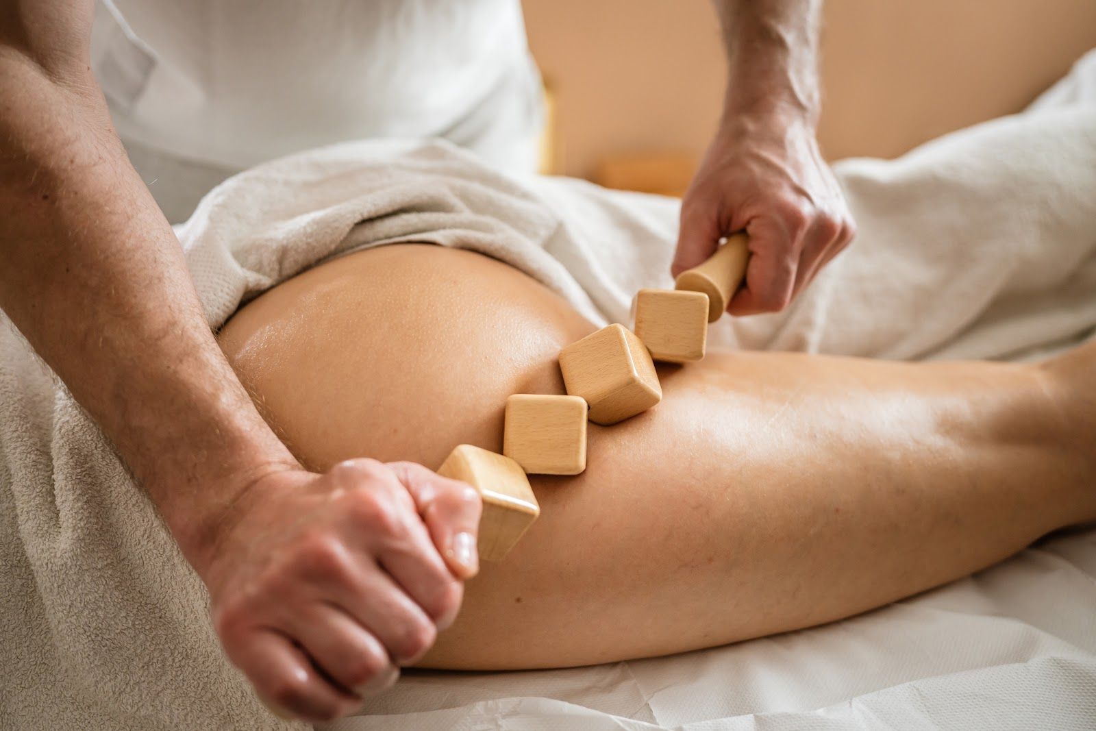 Hands massage a person’s leg with wooden tools in a spa setting