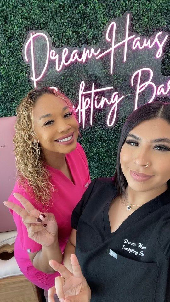 Two women are posing for a picture in front of a neon sign.