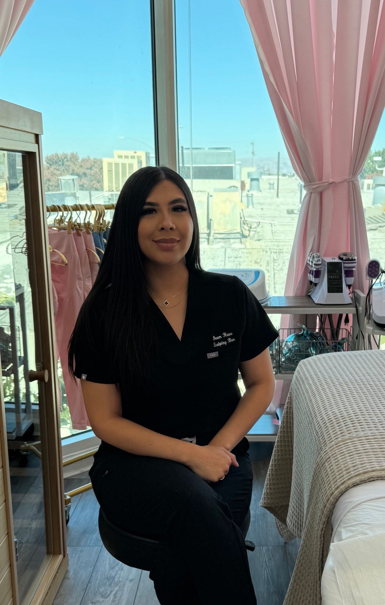 stella in scrubs is sitting on a stool in front of a window in a room.