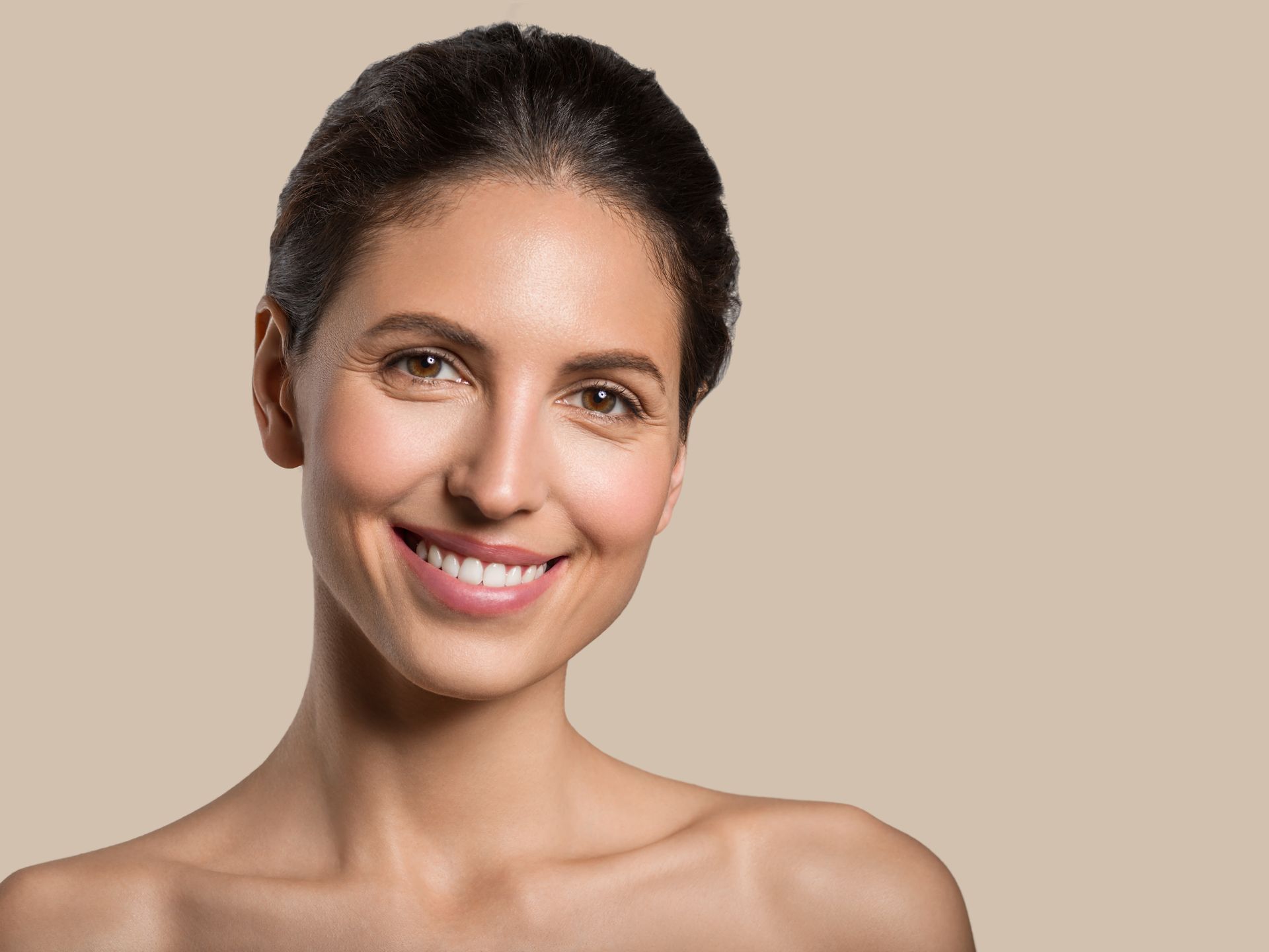 A woman wrapped in a towel is touching her neck and smiling.