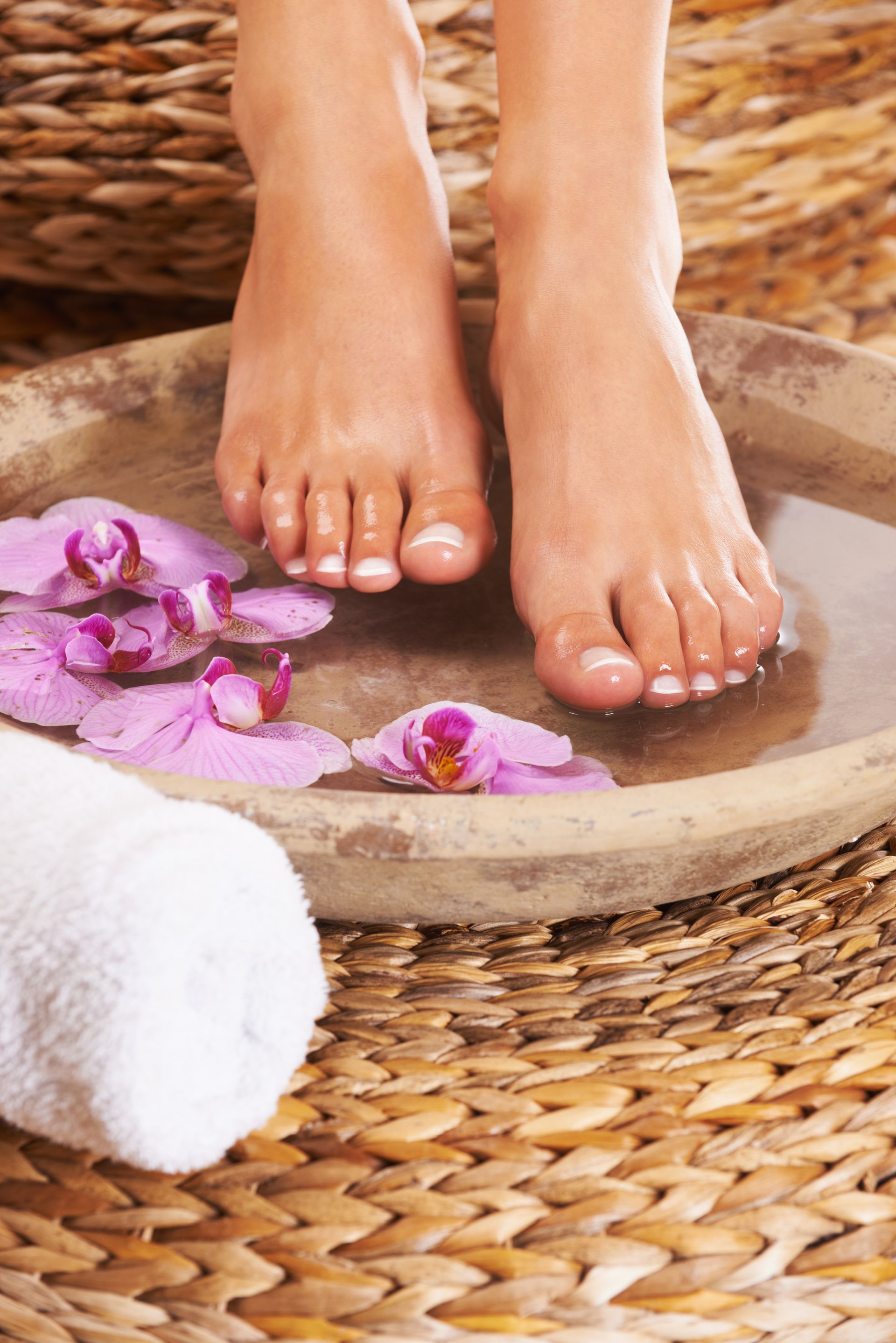 A woman 's feet are in a bowl of water with flowers.