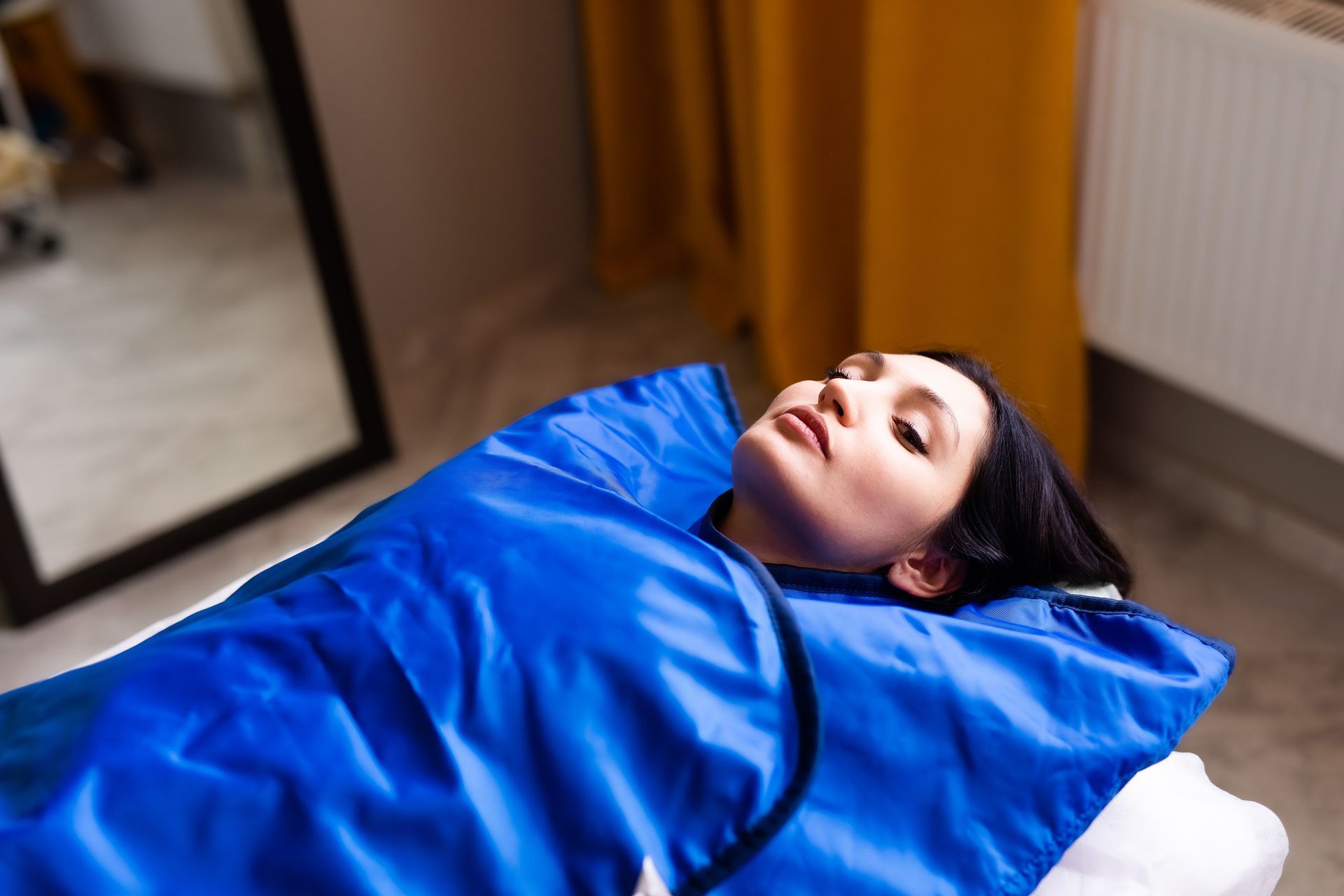 A woman is laying on a bed wrapped in a blue blanket.