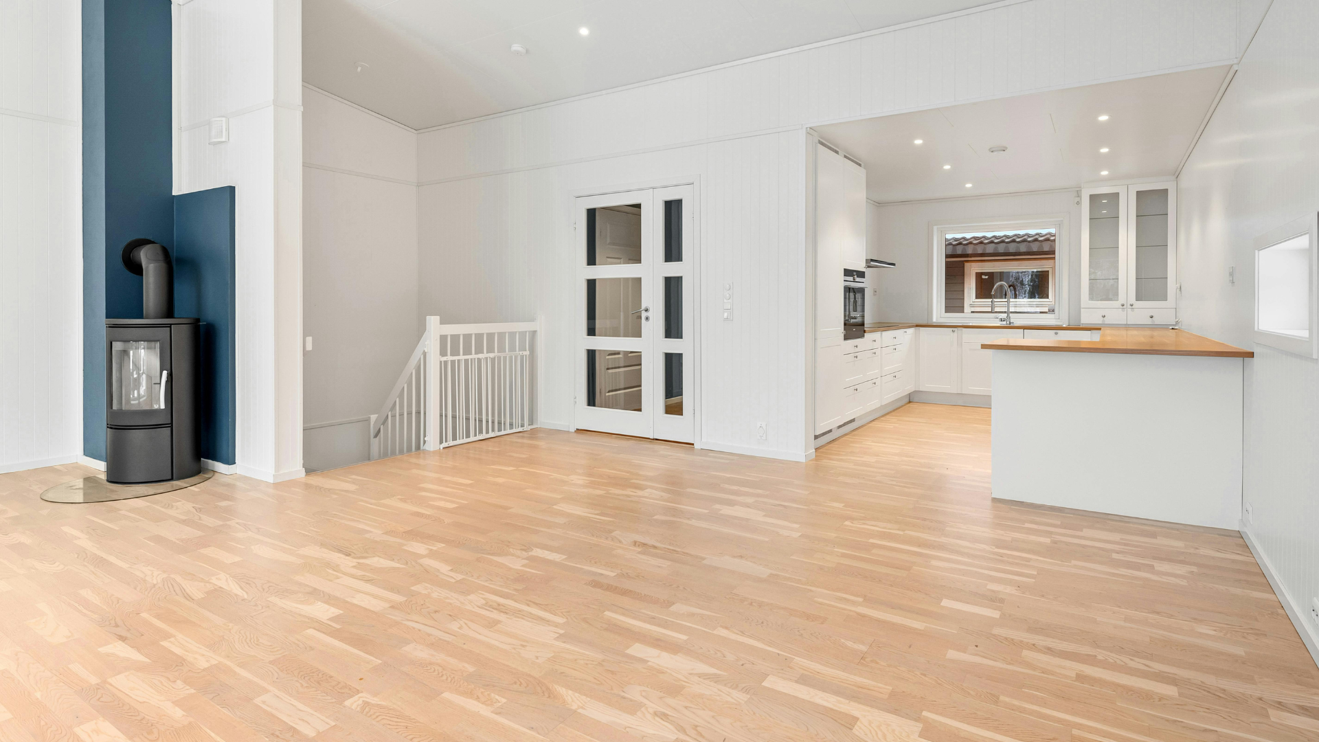Empty living room with hardwood floors, brick fireplace, and white walls