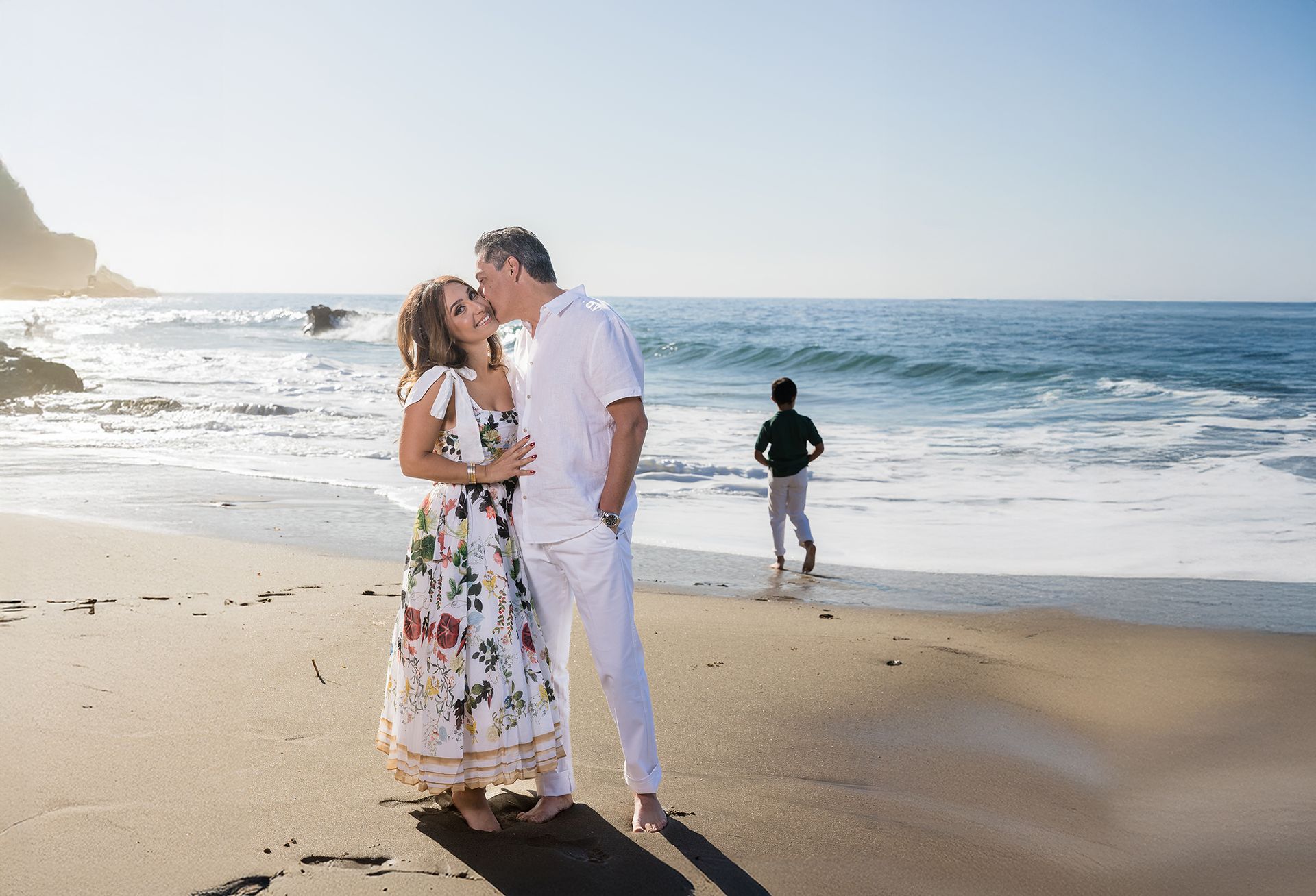 Luxury family photo shoot in Laguna Beach a the base of the cliffs along Heisler Park. Family is wearing green and white outfits.