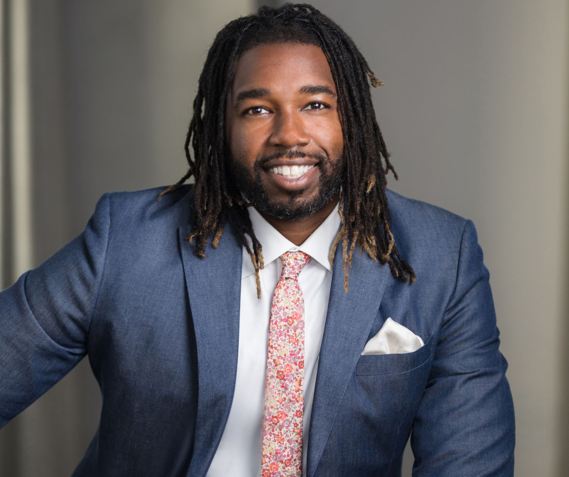 A man with dreadlocks is wearing a blue suit and tie.