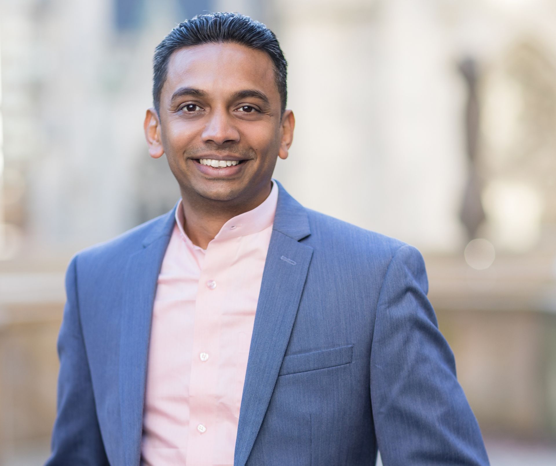 A man in a suit and pink shirt is smiling for the camera.