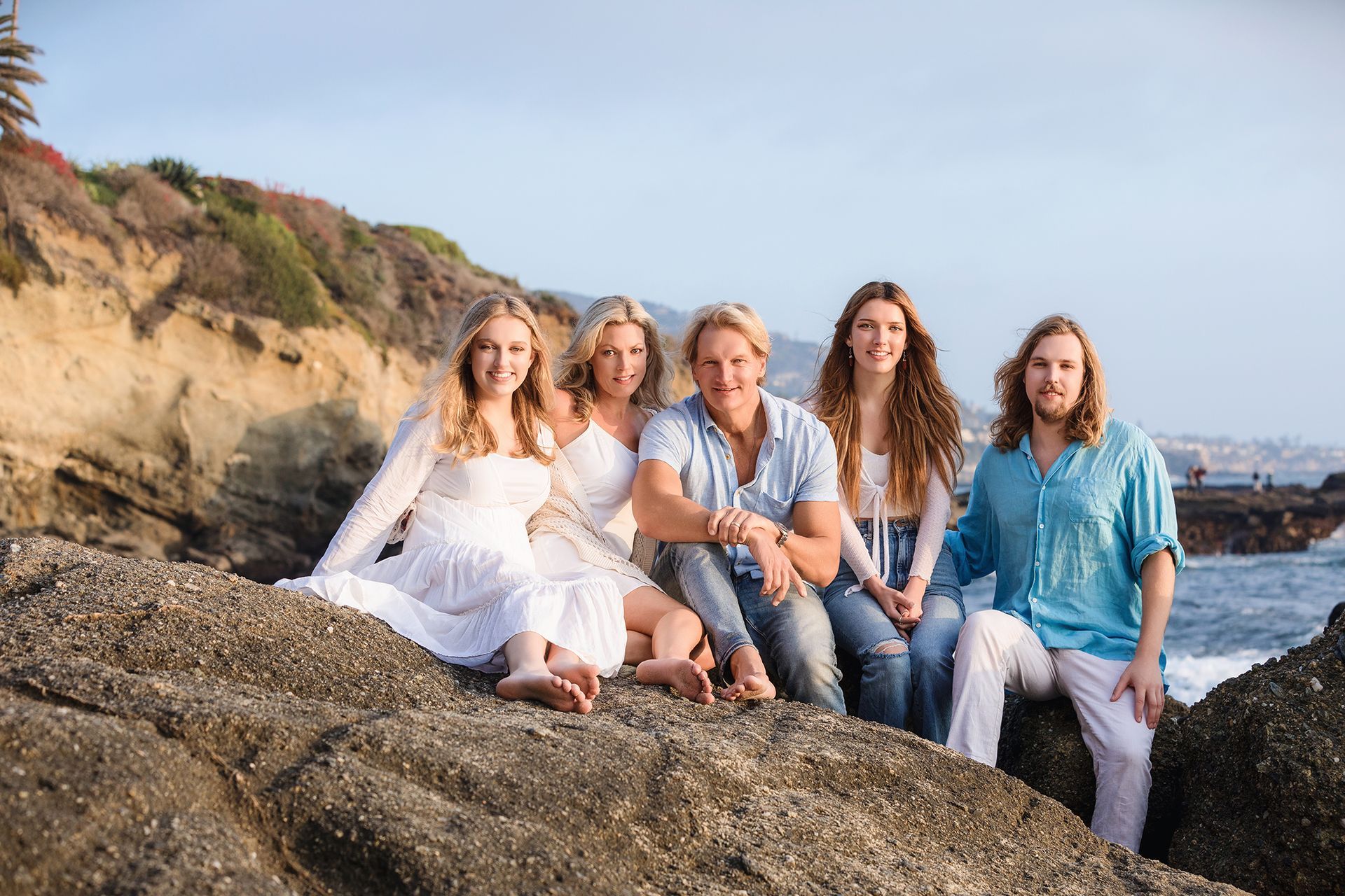 A family is sitting on a rock near the ocean.