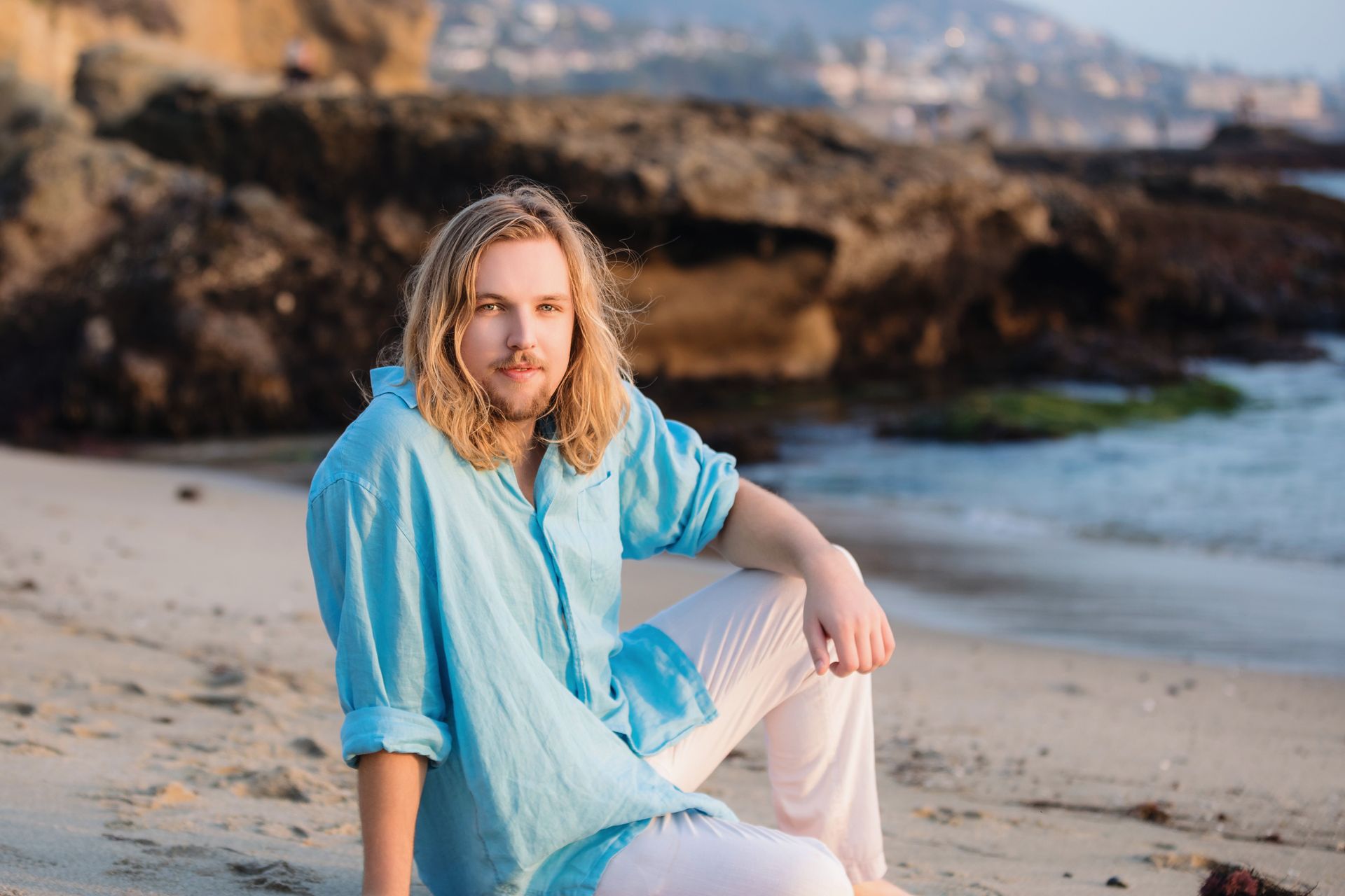 A man is sitting on the beach wearing a blue shirt and white pants at Goff Point in Laguna Beach.