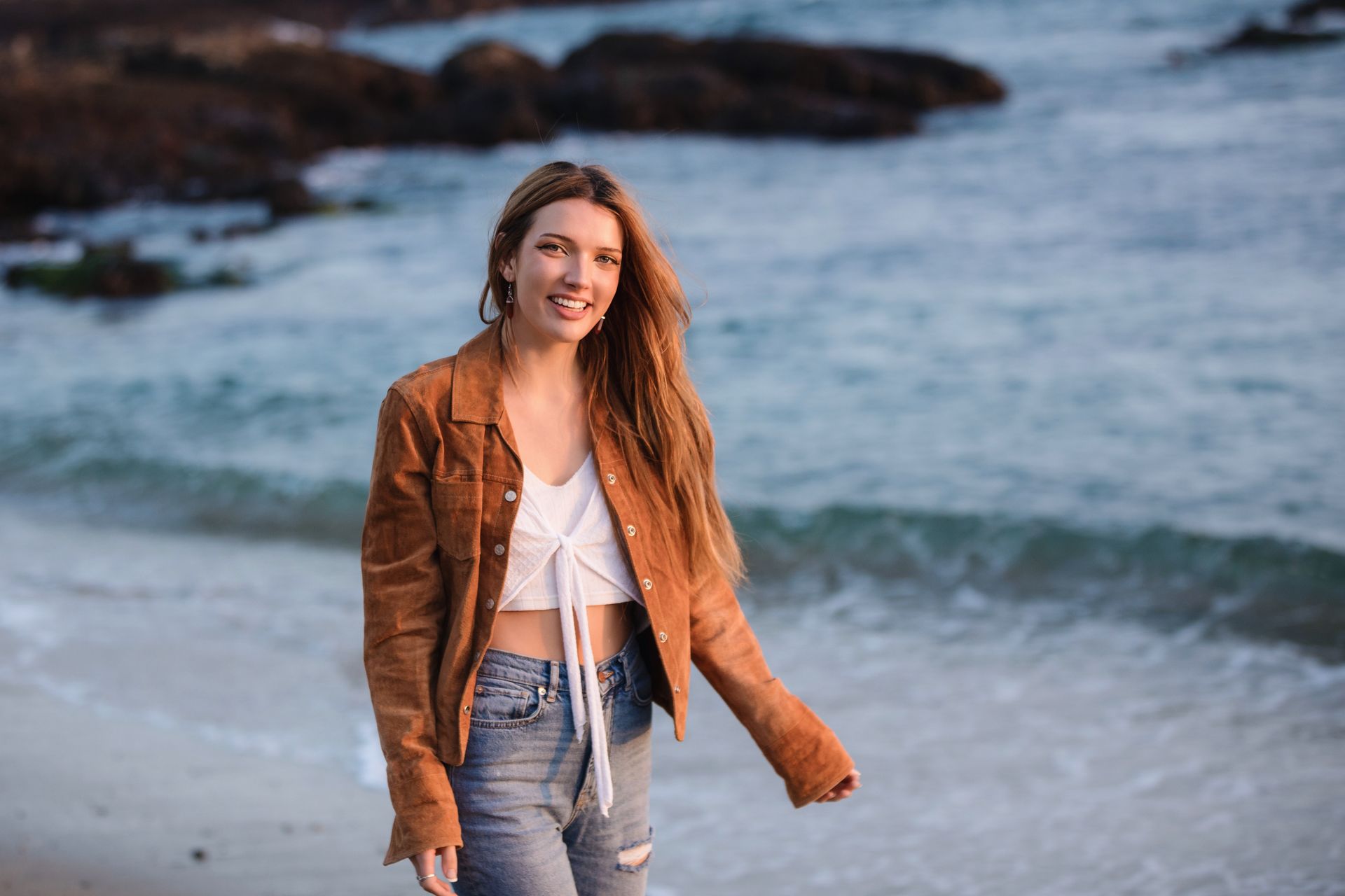 A woman in a brown jacket is walking on the beach.