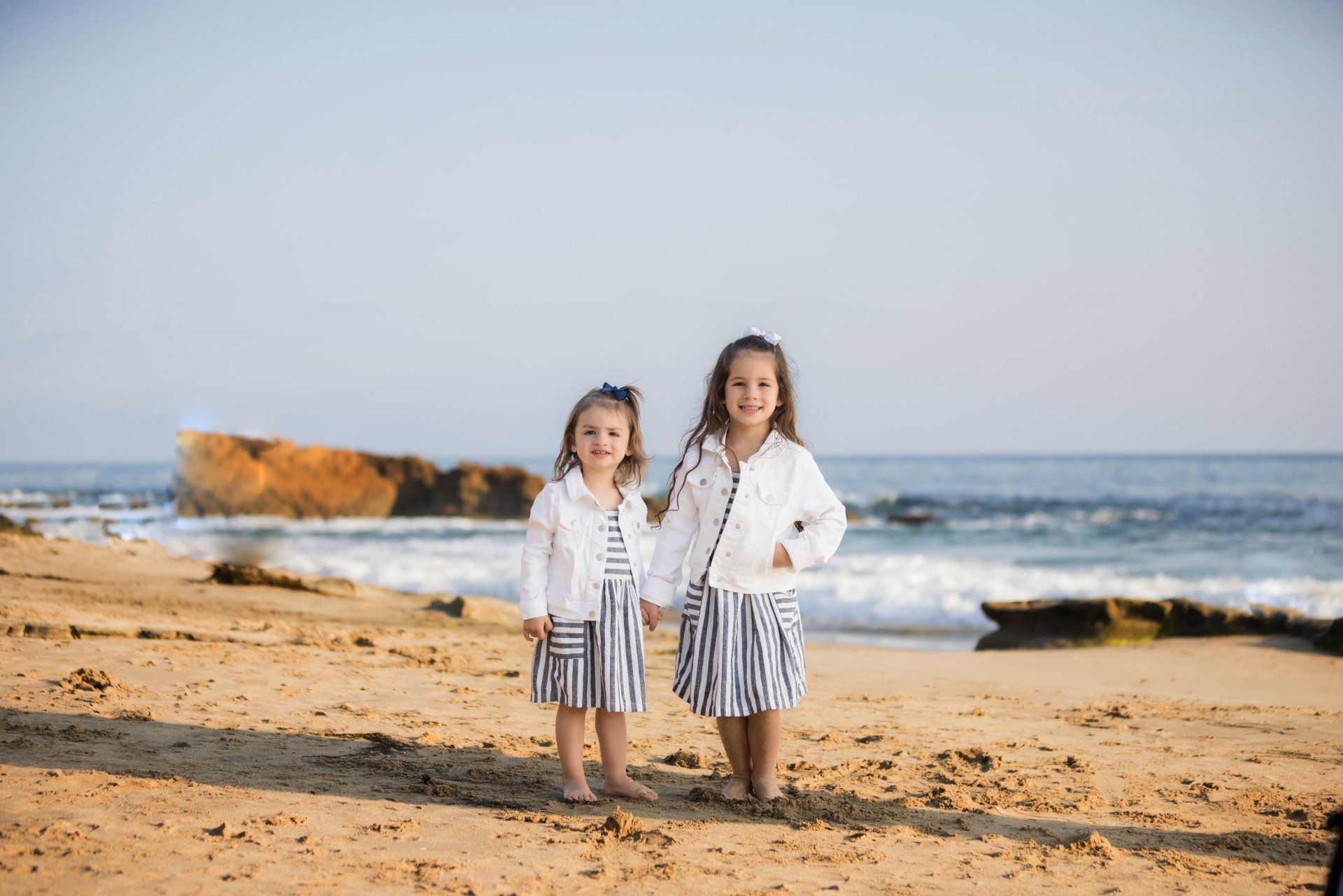 Two little girls are standing on a beach holding hands.