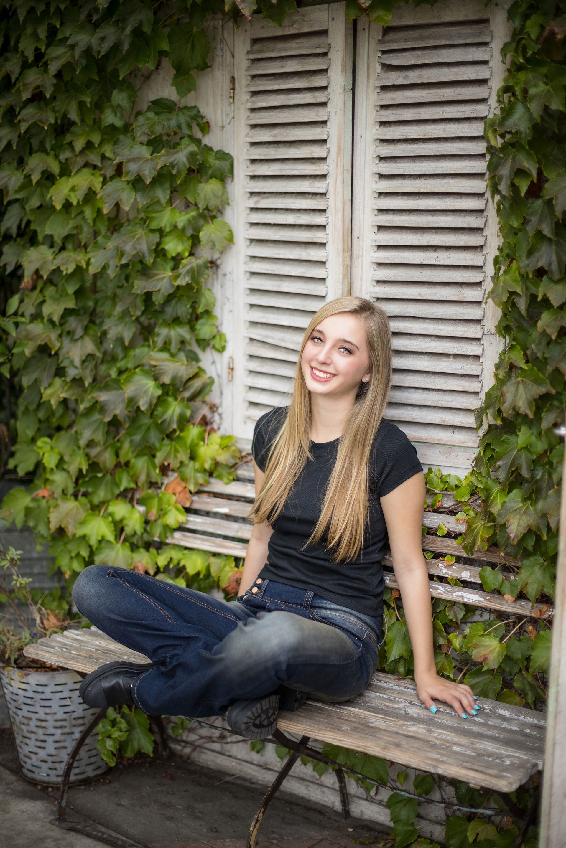 Senior girl seated on a bench under shutters at The Camp in Costa Mesa